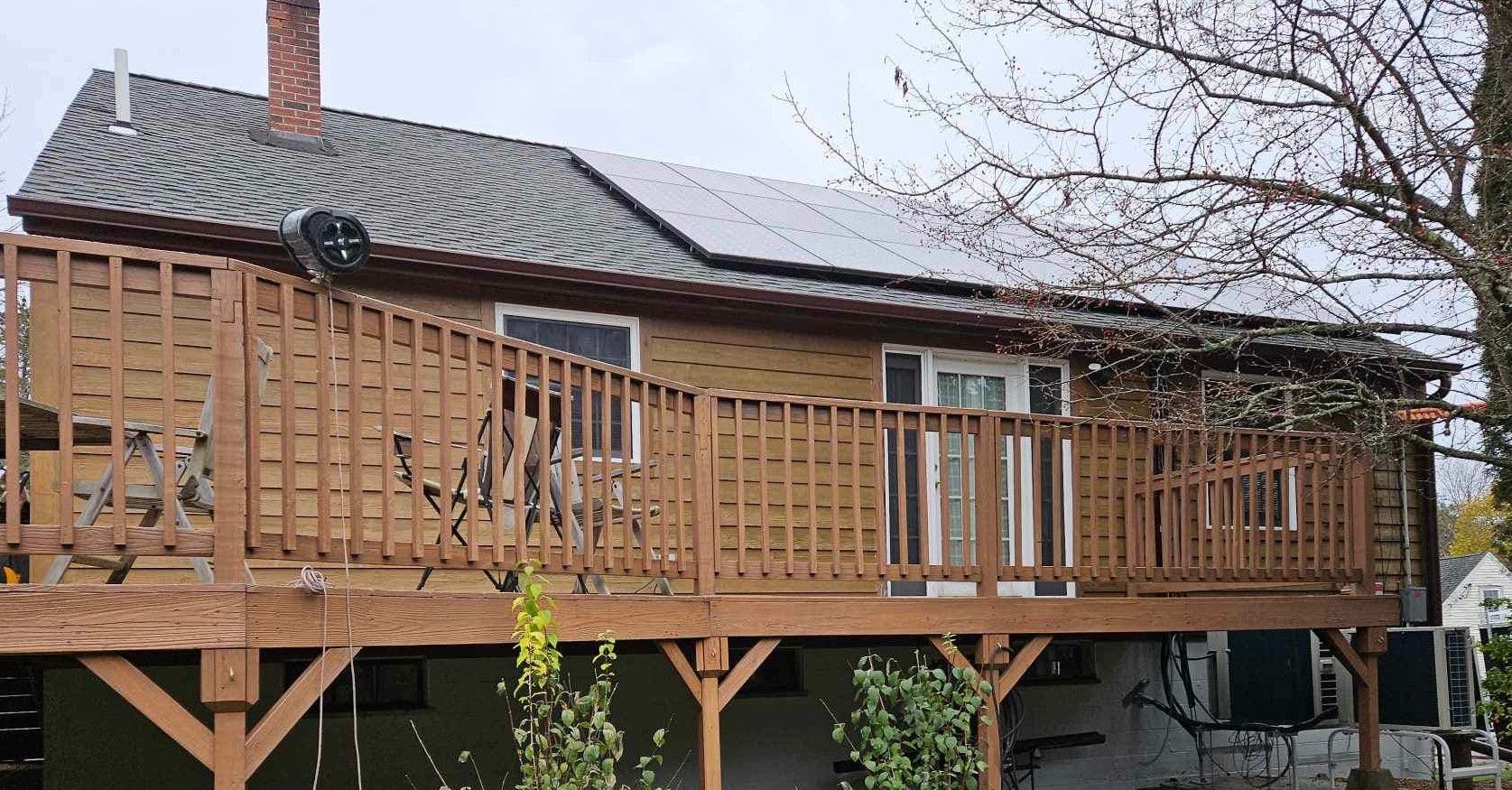 House with brown siding, deck, and solar panels on the roof, under a cloudy sky.