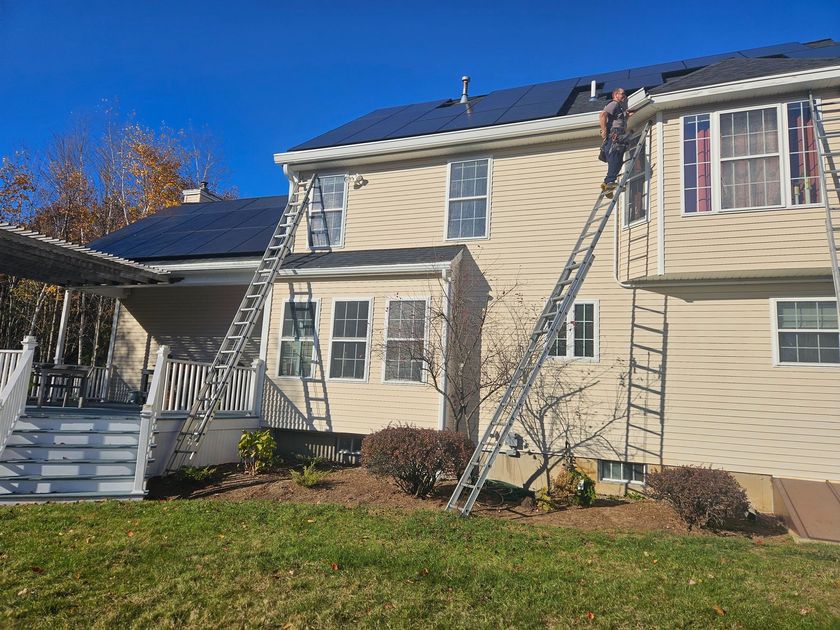 New England Gutter Systems crew installing 8-inch K-style gutters and snow stops on a Bedford NH home with solar panels