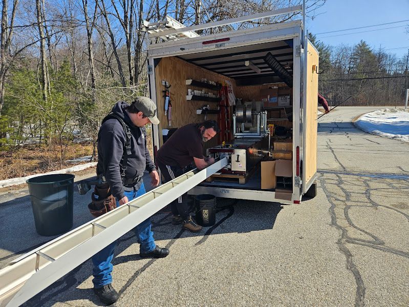 Two workers with a trailer on a sunny day, preparing a long metal gutter.