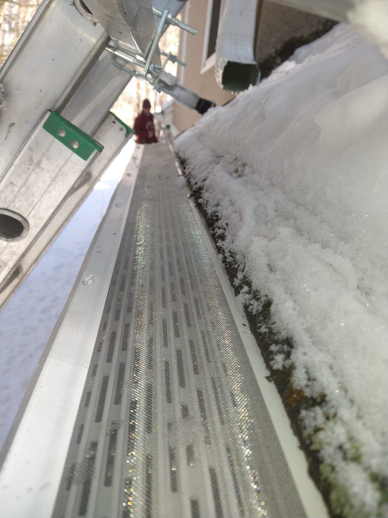 Ladder next to a gutter partially filled with snow. Person near the gutter.