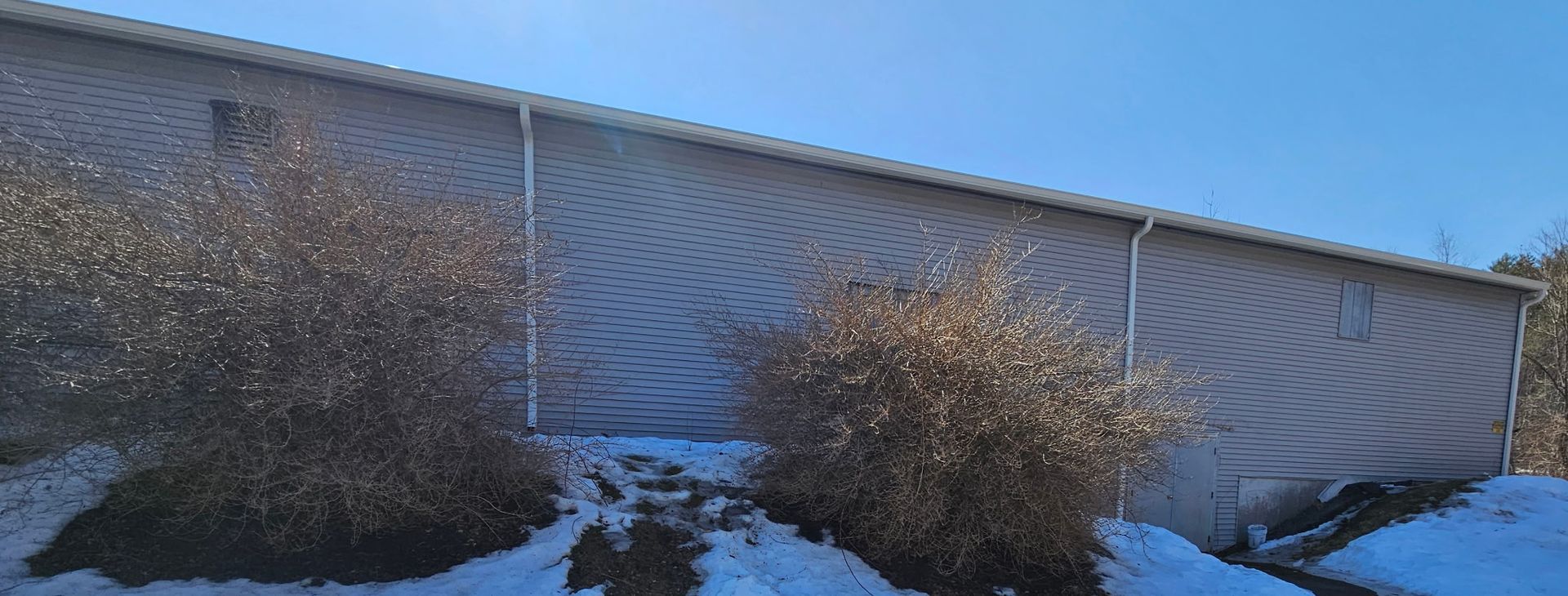 New England Gutter Systems installing six inch seamless aluminum gutters on Monadnock Tennis Club commercial building in Peterborough NH with additional downspouts for improved drainage