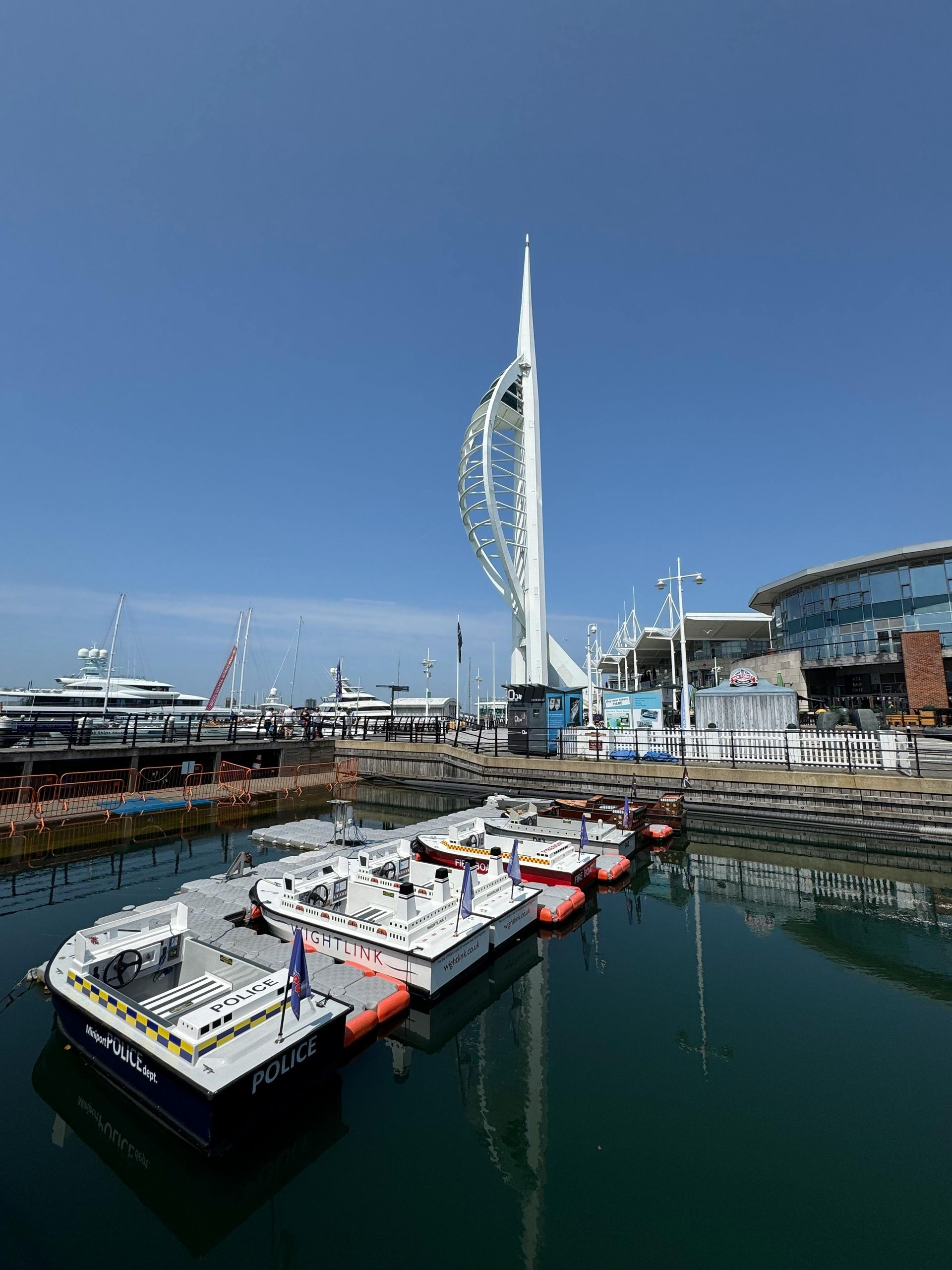 Boats docked in water, the Spinnaker Tower in the background, bright blue sky. Portsmouth, UK.