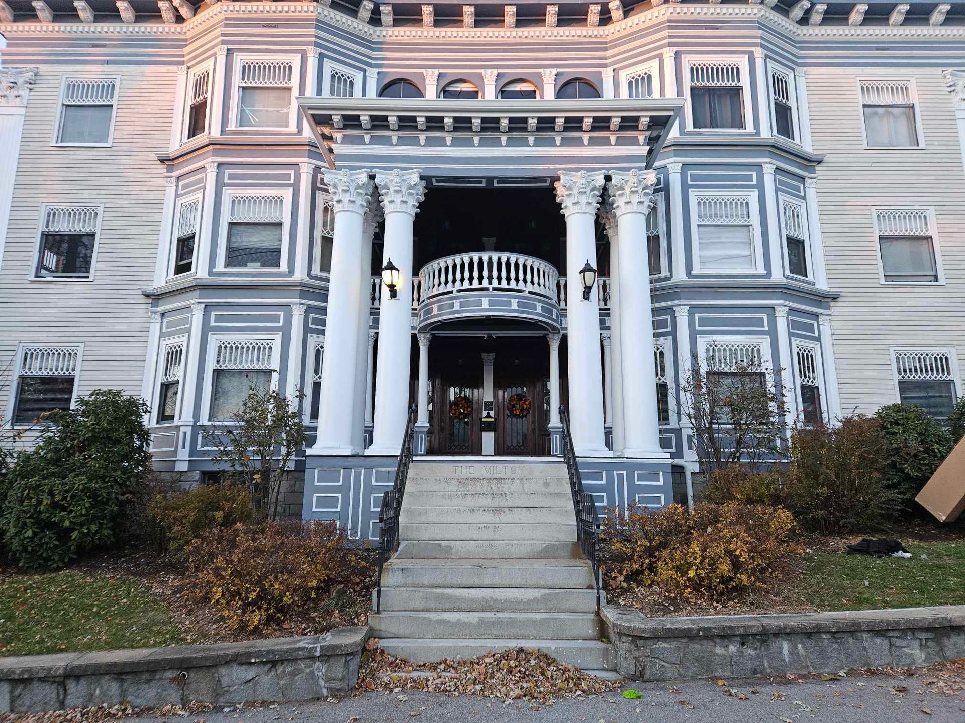 Gray Victorian building with a columned entrance, steps, and a small balcony.