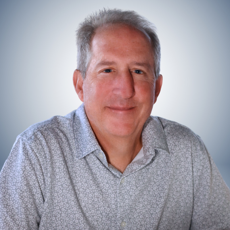 Man with gray hair, wearing a patterned button-down shirt, smiles at the camera against a gradient background.