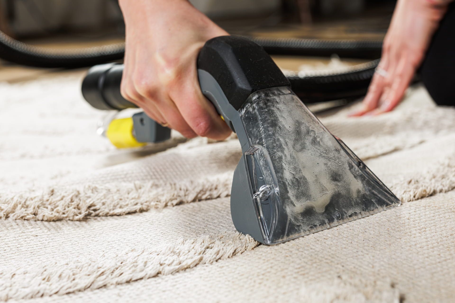 Hand using a carpet-cleaning tool to lift dirt from a beige rug on the floor