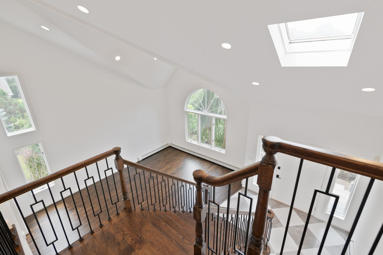 High-angle view of a staircase, featuring dark wood, black railing, and white walls with a skylight.