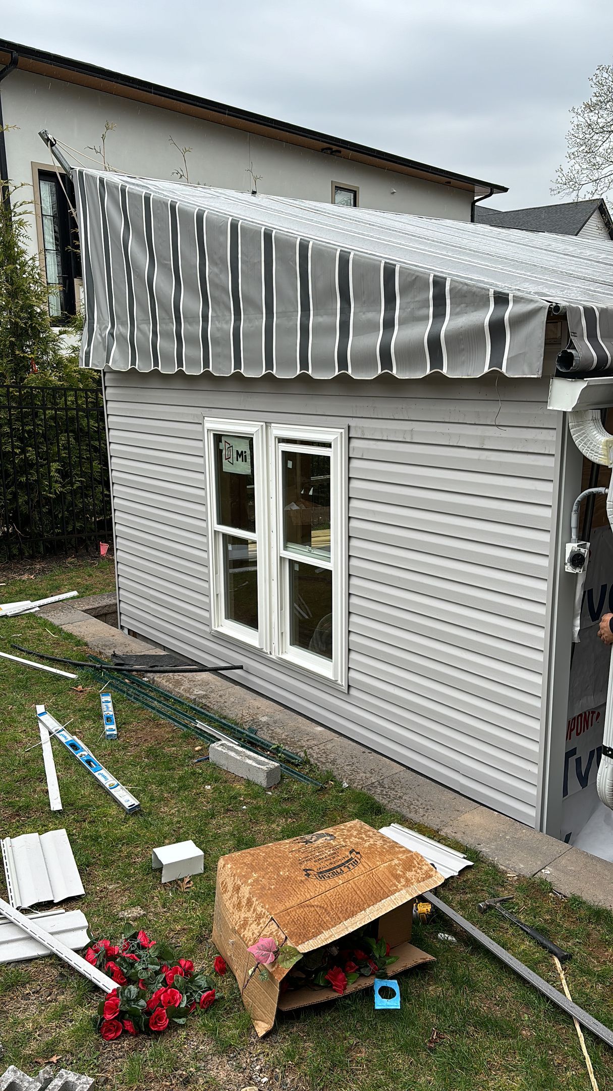 Exterior of a building under construction, featuring gray siding, white window frames, and a partially covered roof.