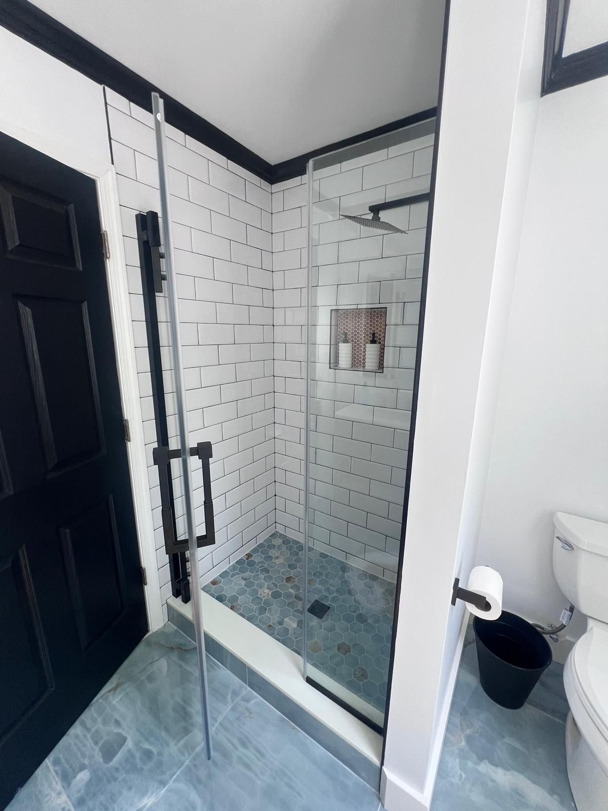 Bathroom with a glass shower, white subway tiles, and a black door.