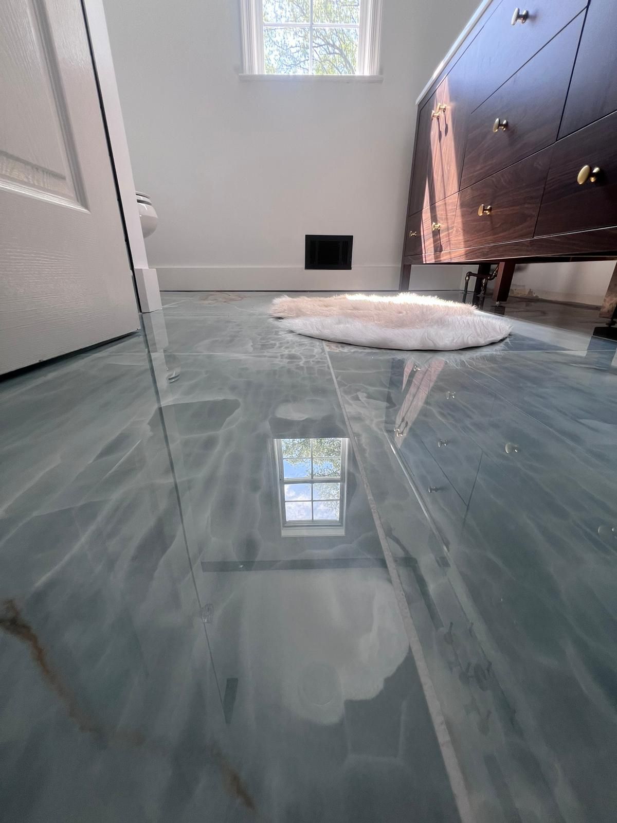 Blue and white swirled epoxy bathroom floor with a small rug, vanity, and window.