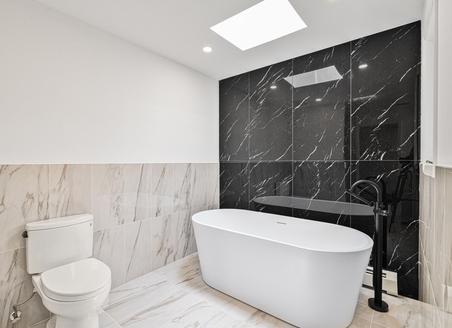Modern bathroom with white tub, toilet, and marble and black tiled walls.