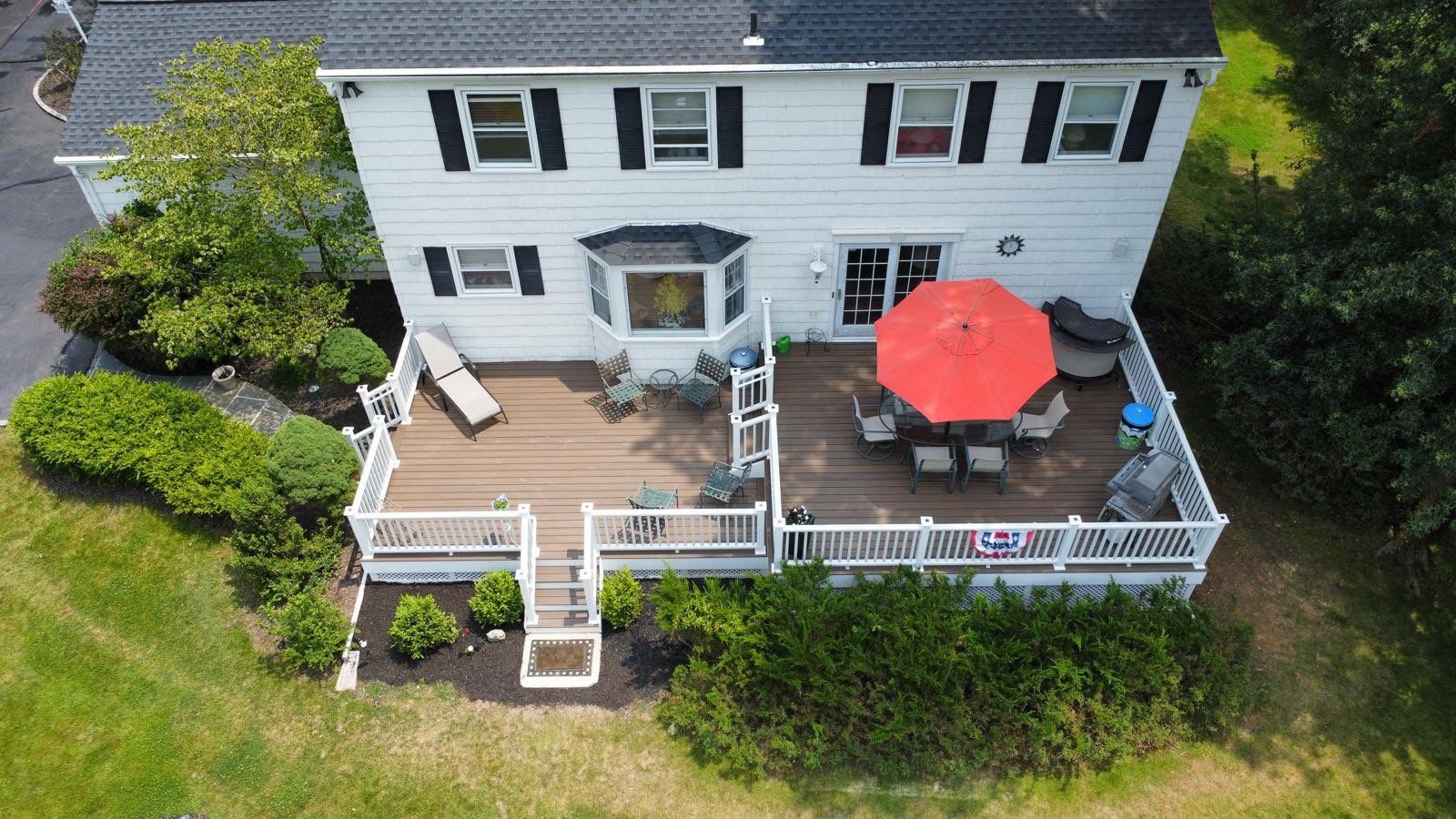 Two-story white house with a deck. A red umbrella shades a table and chairs on the deck.