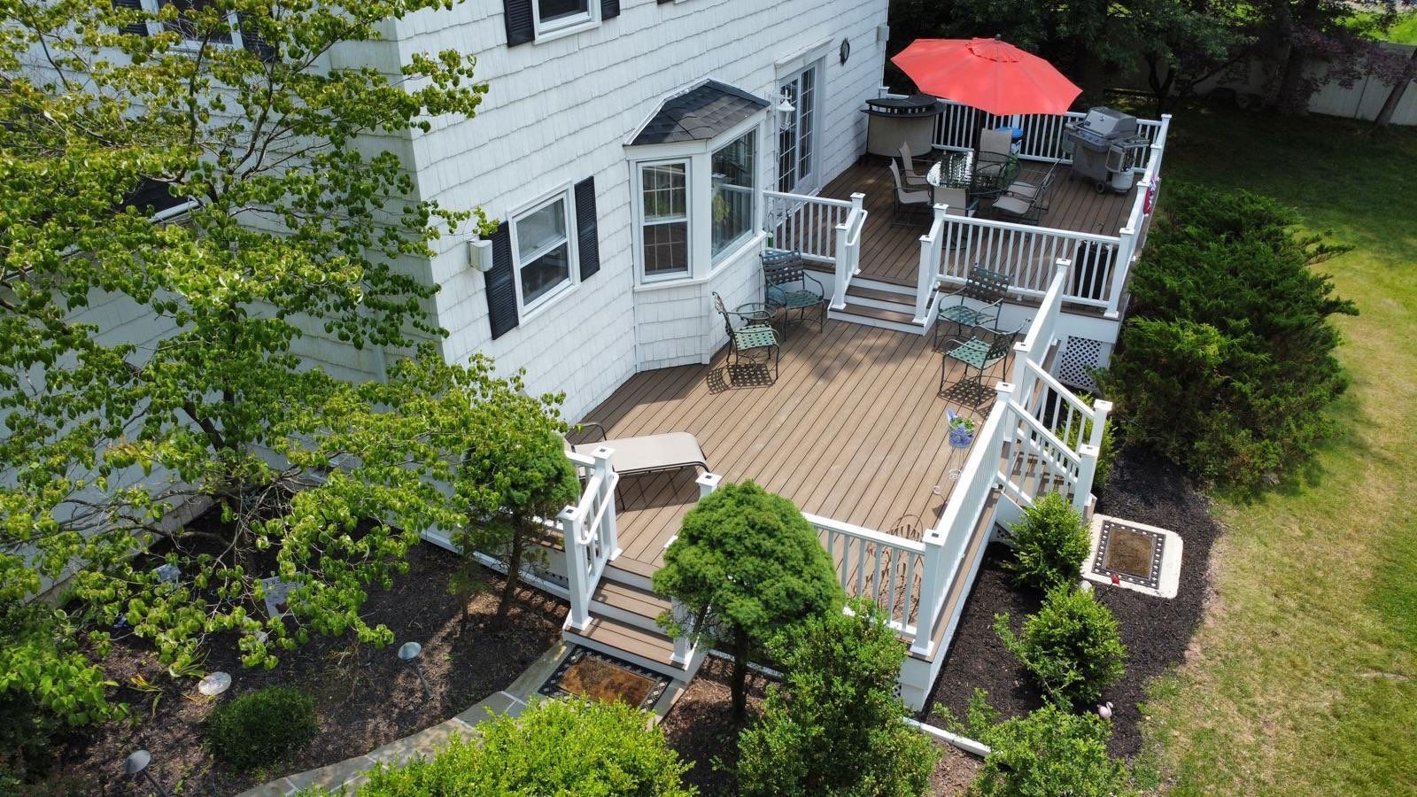 White house with multi-level wooden deck; red umbrella over outdoor seating.