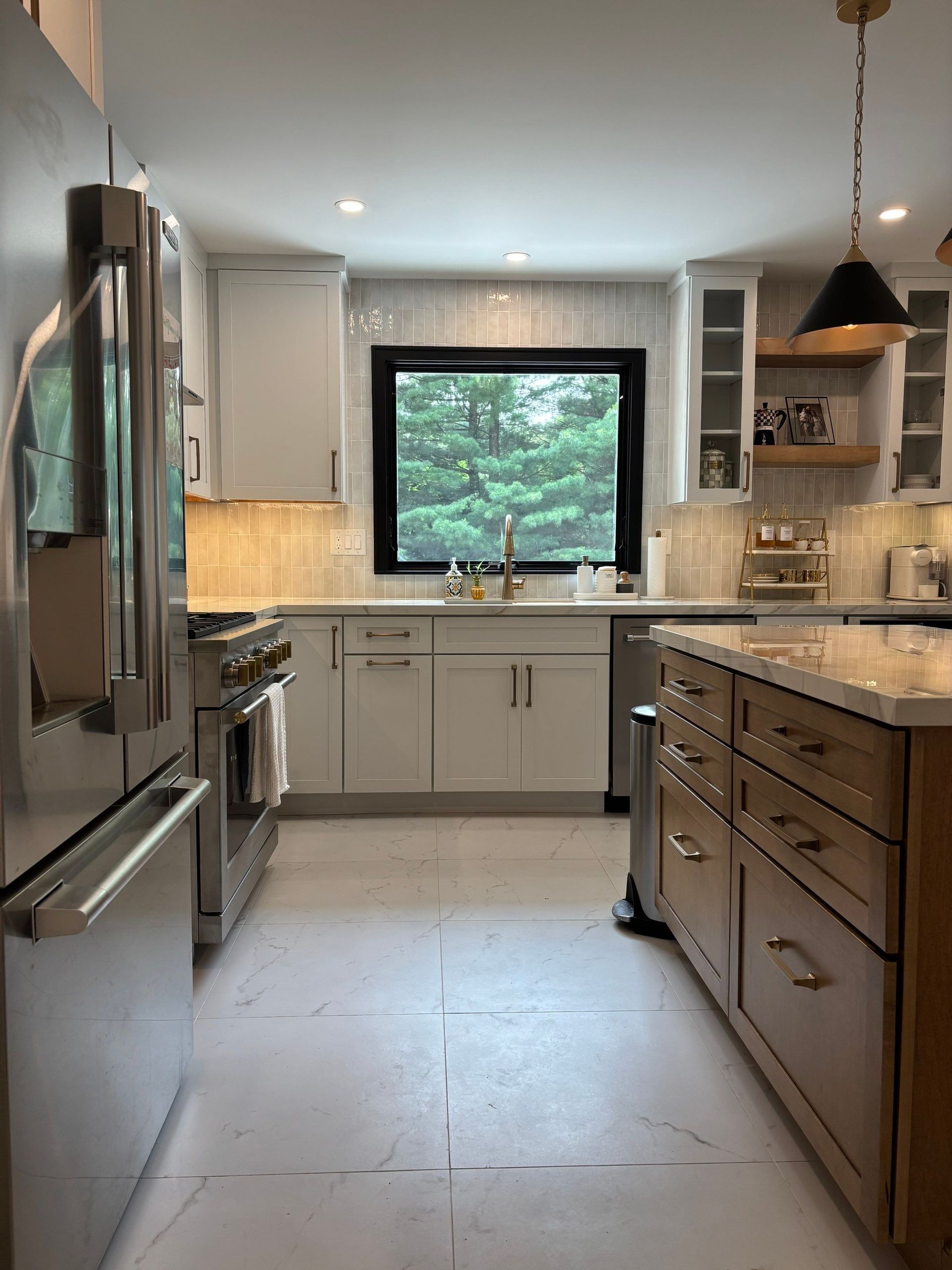 Kitchen with stainless steel appliances, light gray cabinets, and a wood island. A window offers a view of green trees.