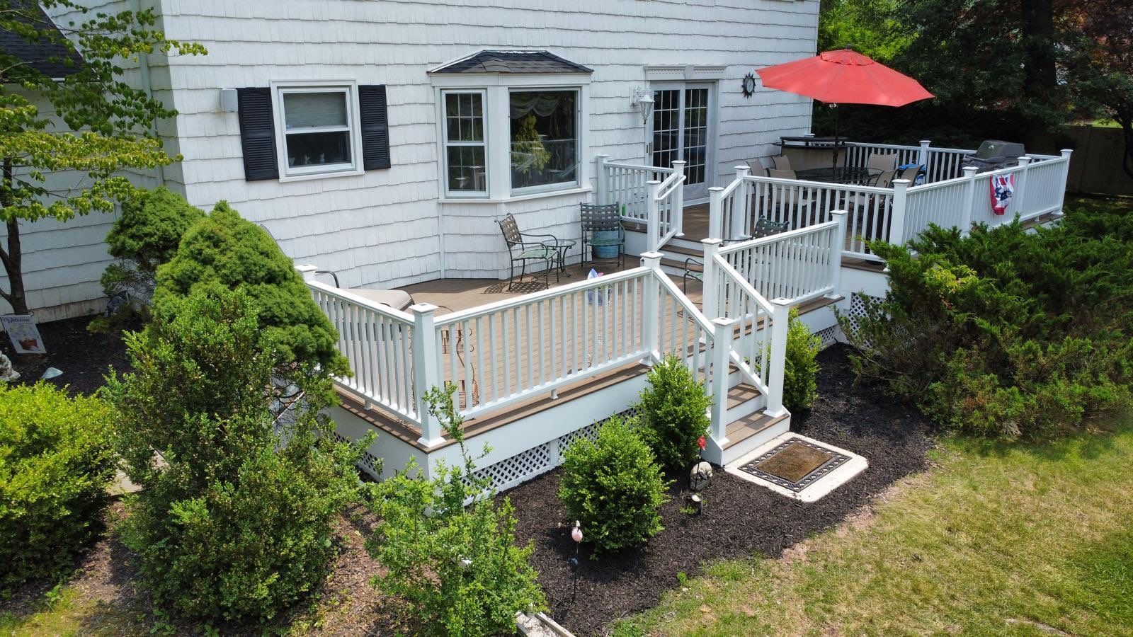 White house with a multi-level wooden deck, red umbrella, and surrounding greenery.
