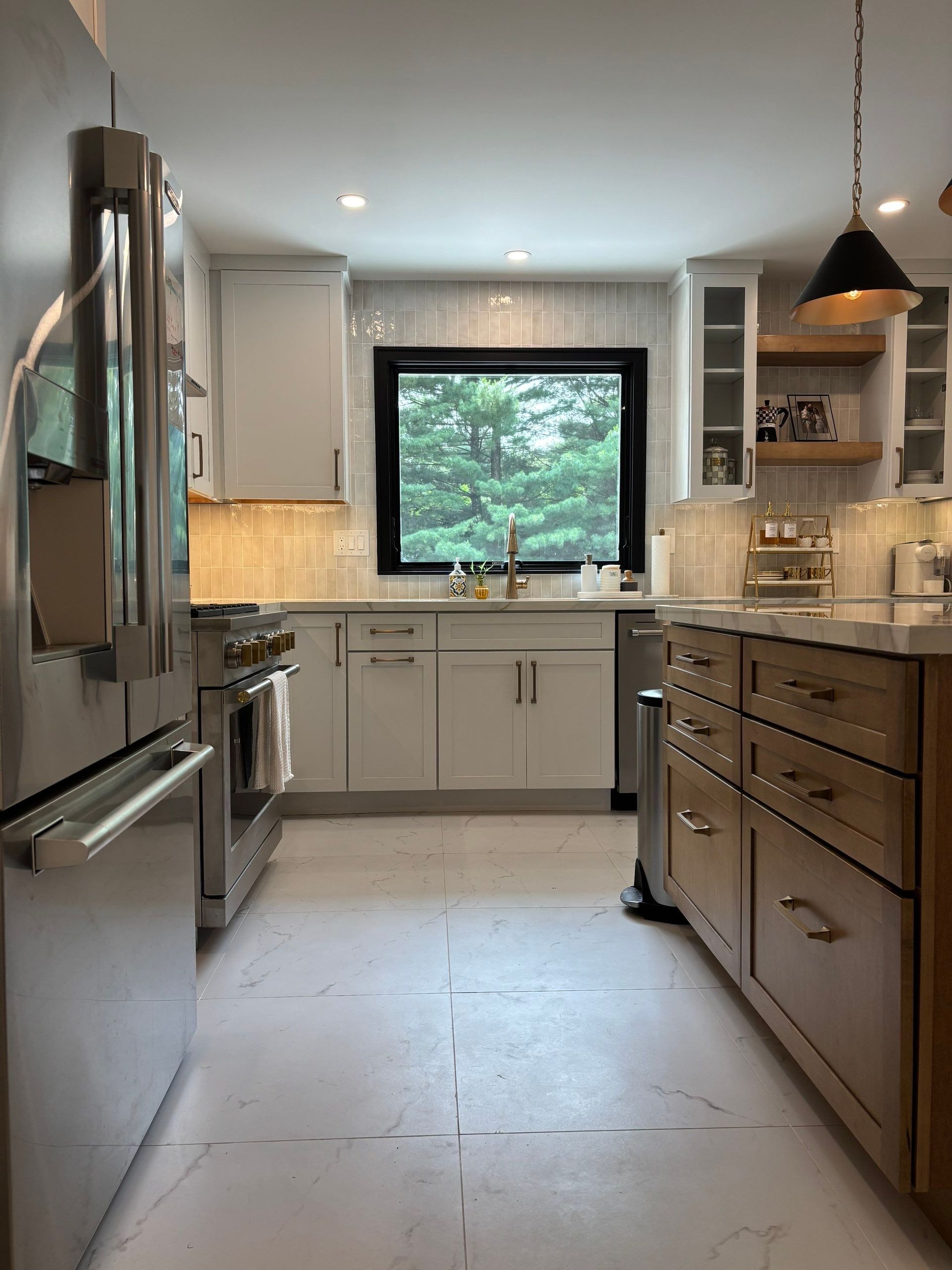 Kitchen with stainless steel appliances, white cabinets, island with wood-tone cabinets, window, and pendant light.