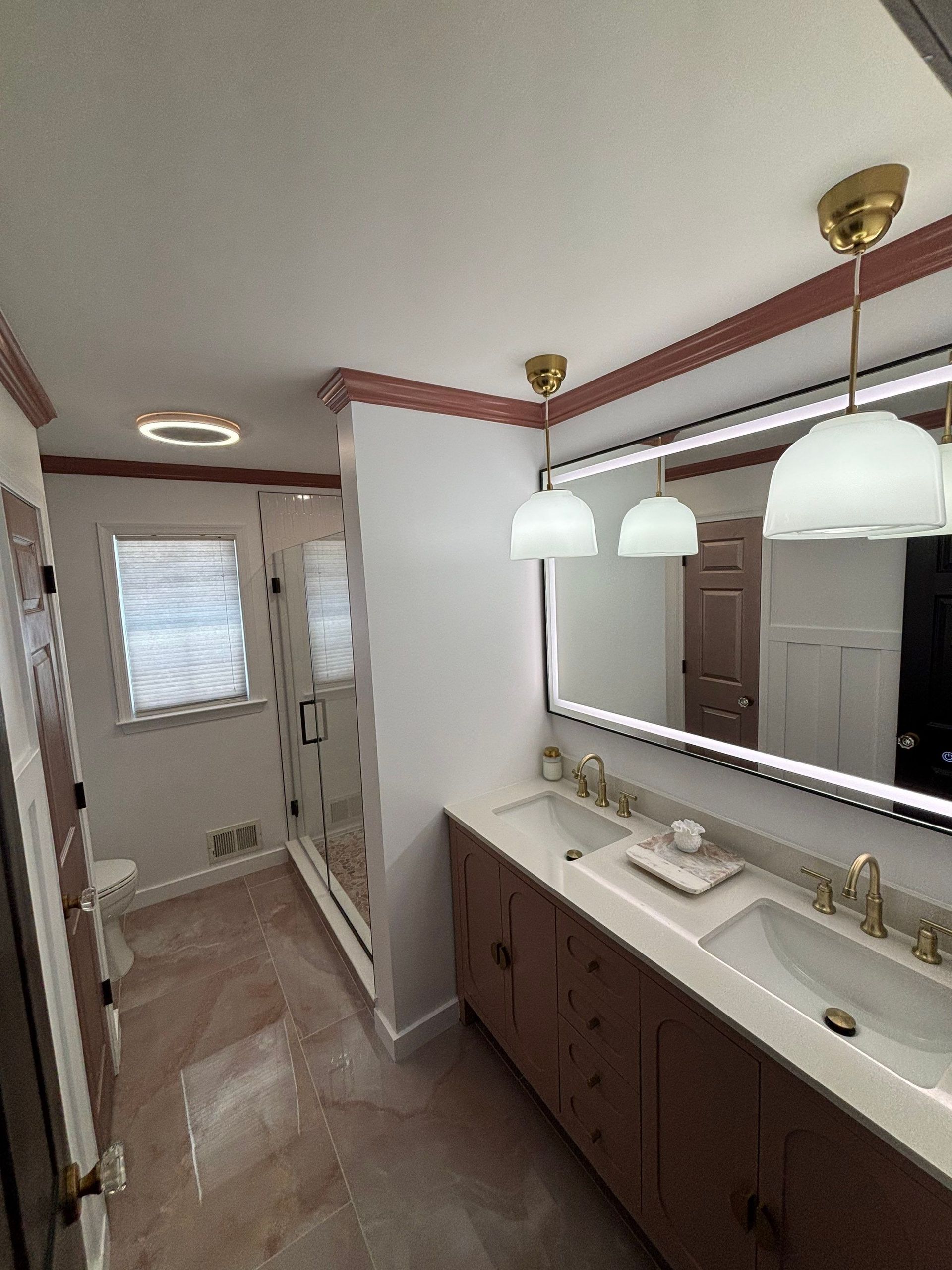 Bathroom with double vanity, large mirror, and shower stall. Features include pink tile, gold accents, and pendant lights.