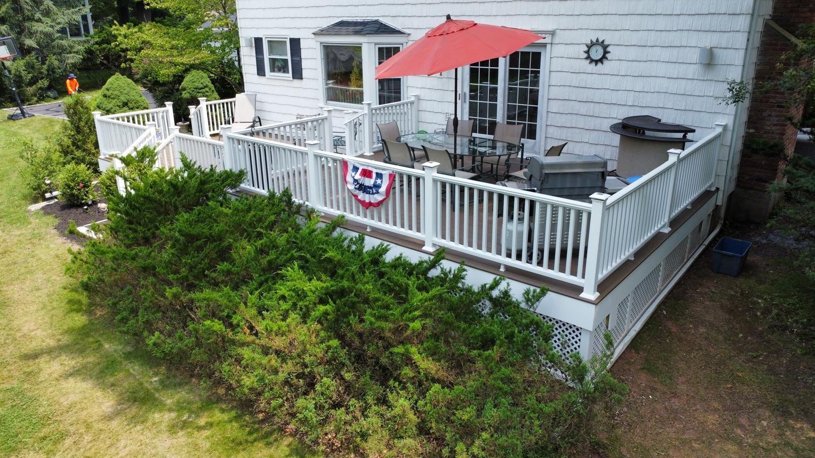 White house with a deck featuring a table with umbrella, grill, and American flag decoration.