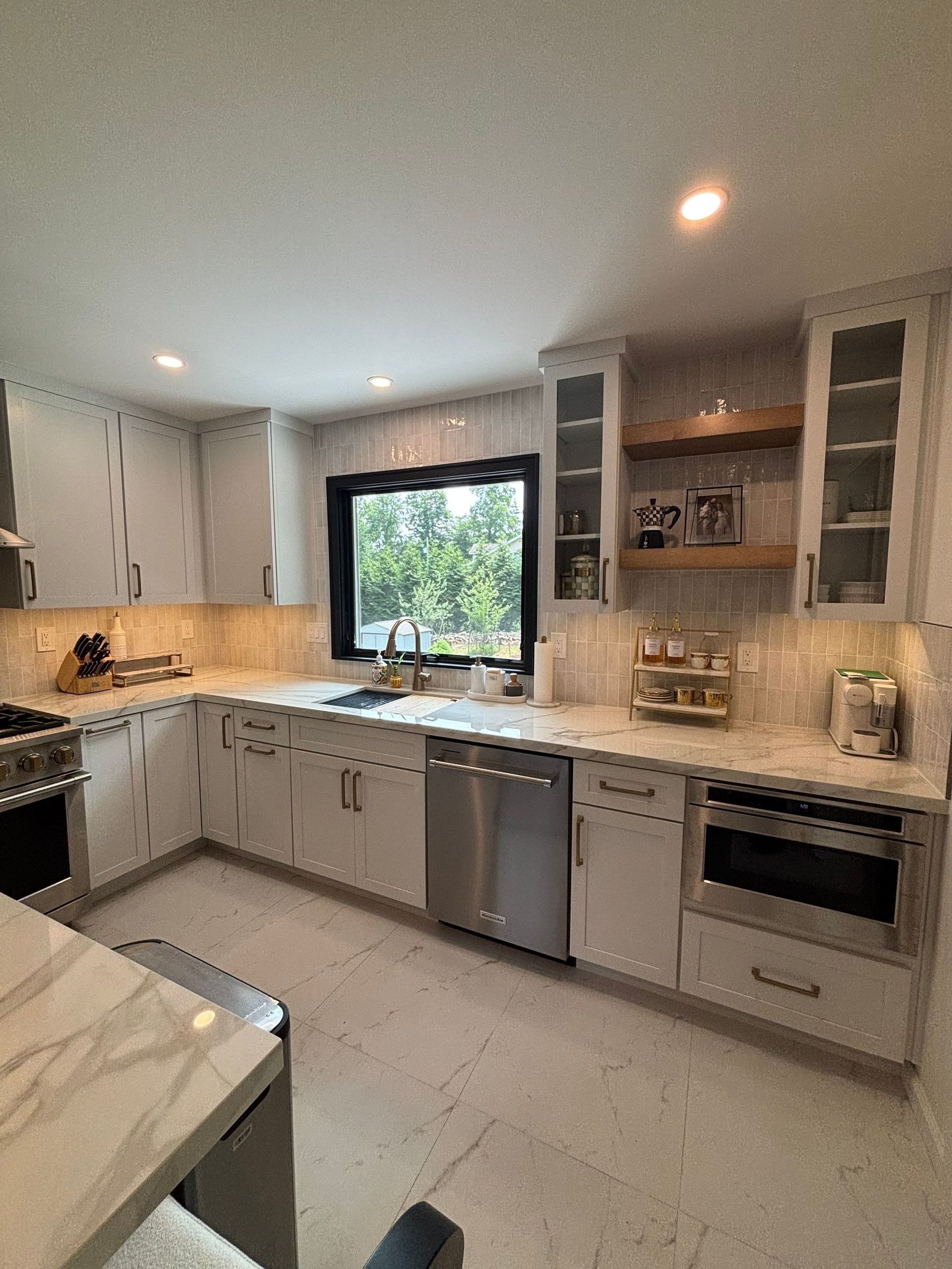 Bright white kitchen with stainless steel appliances, marble countertops, and a large window.