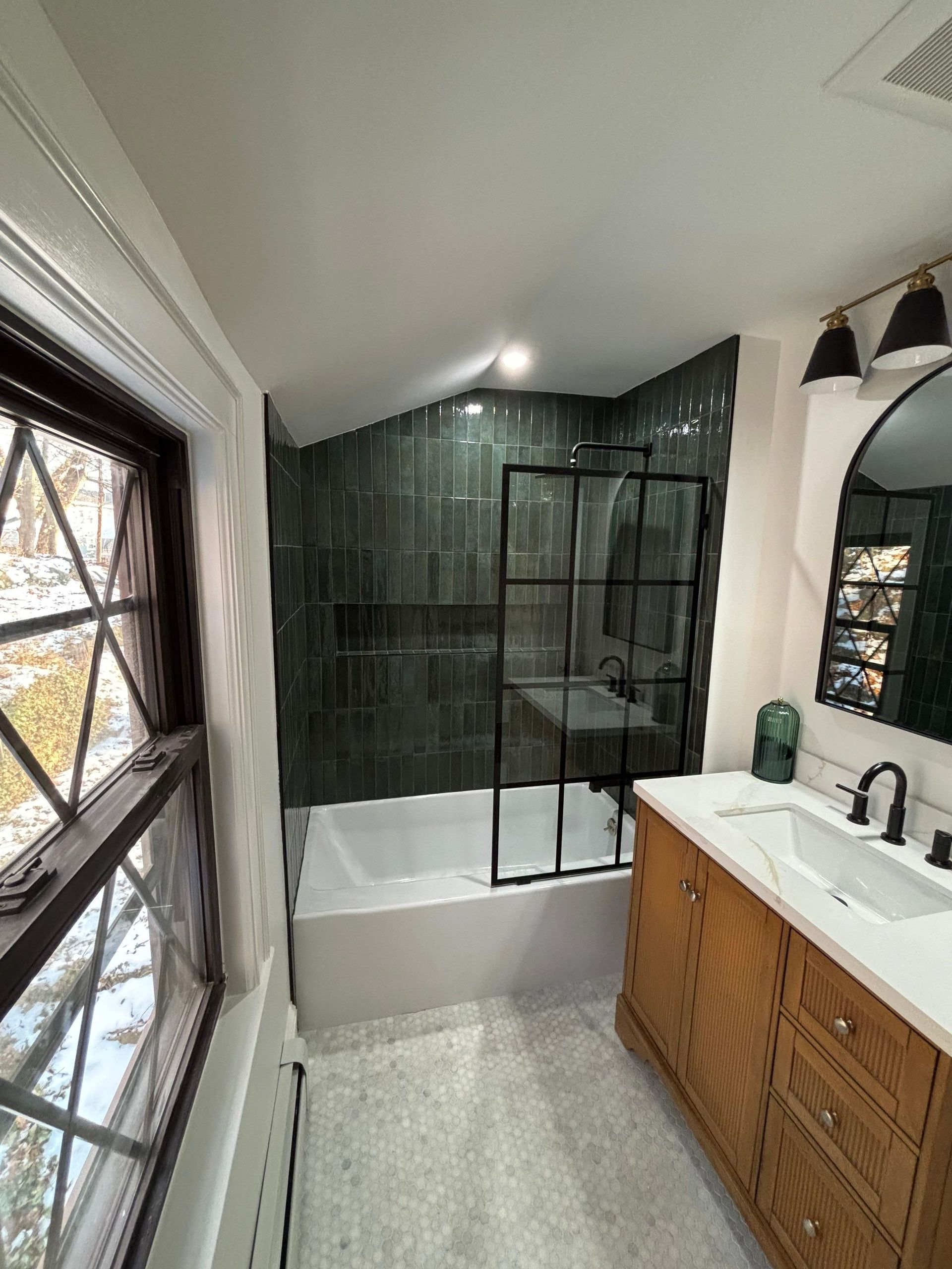 Bathroom renovation with teal tiled shower, wooden vanity, and black framed shower door.