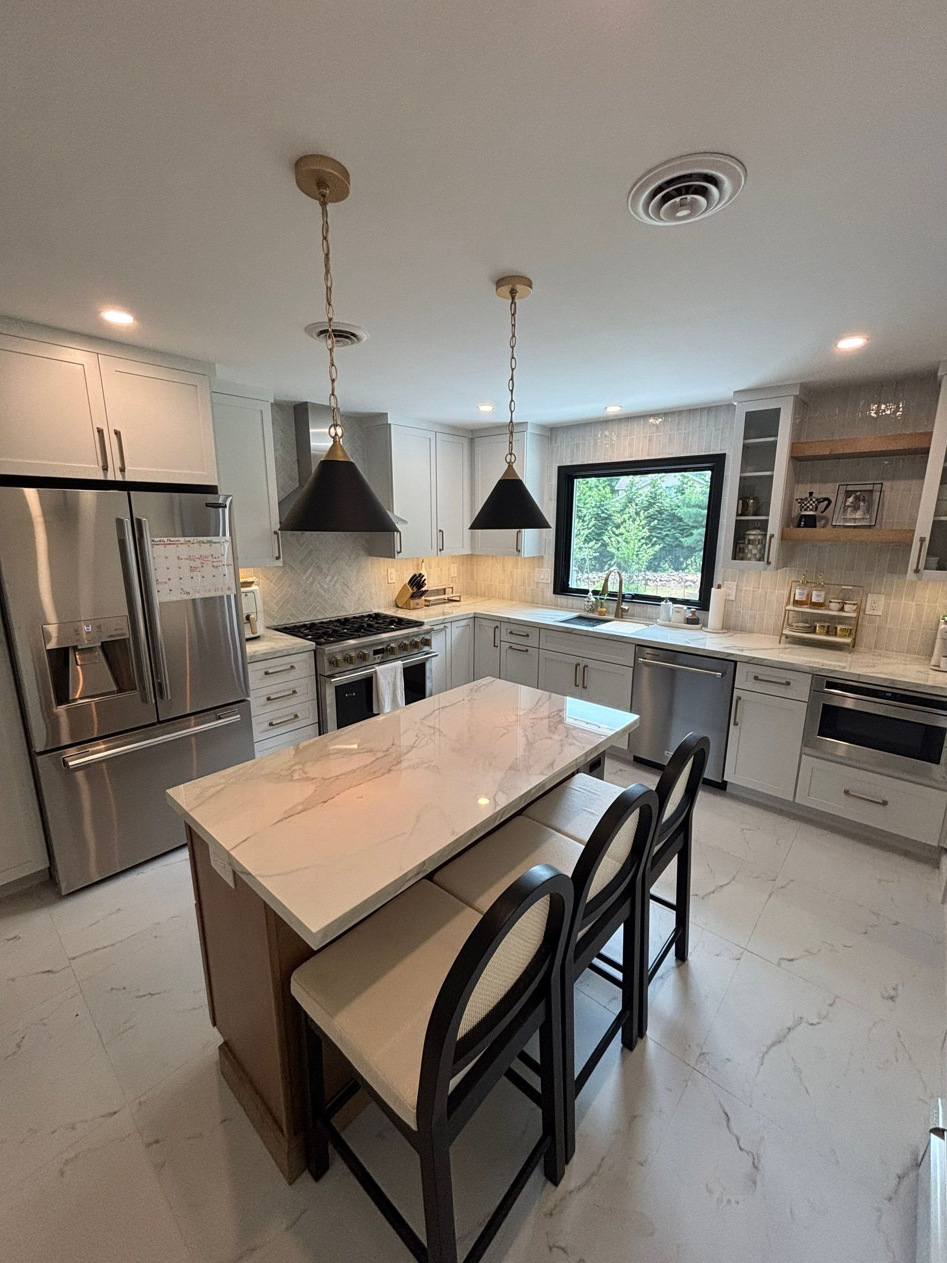 Modern kitchen with island, marble countertop, pendant lights, and stainless steel appliances.