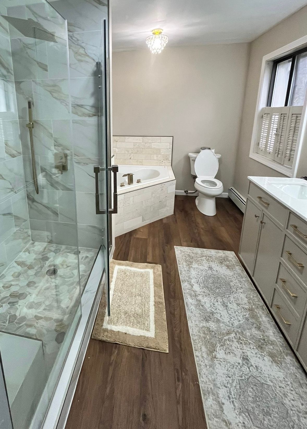 Bathroom with a glass shower, a tub, a toilet, and a vanity, with wooden floors.