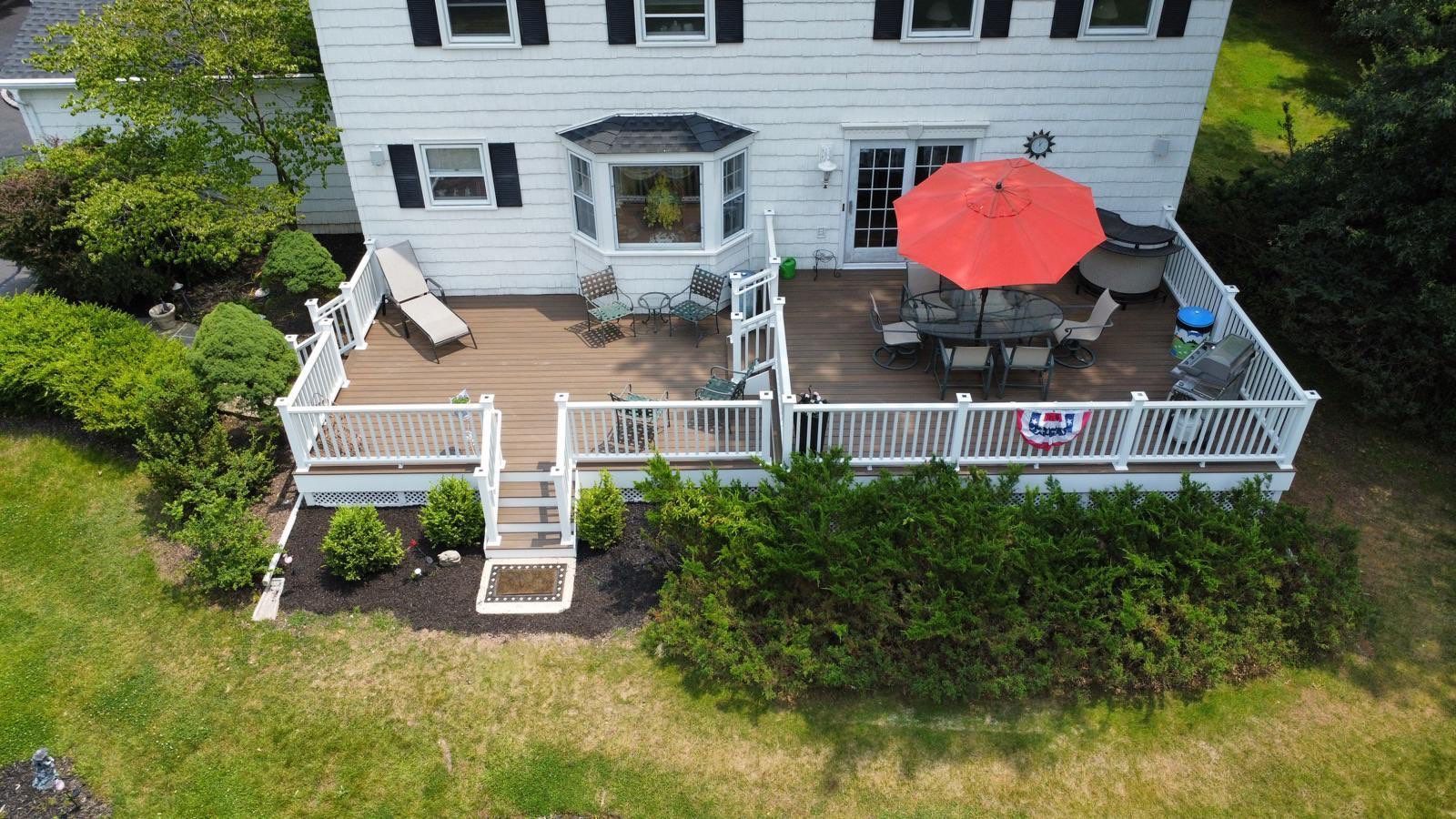 Aerial view of a white house with multiple decks. One deck has a red umbrella and dining set.