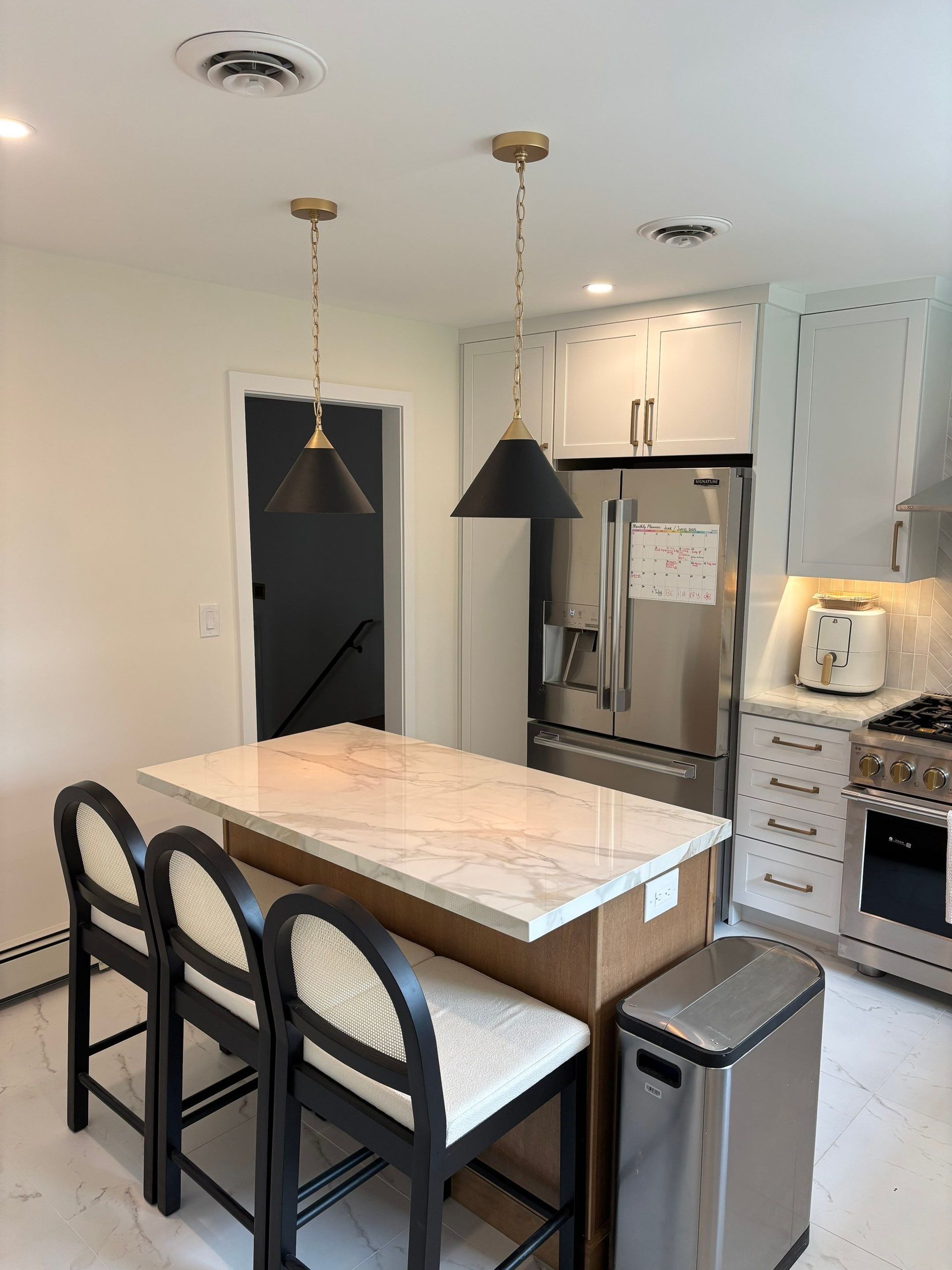 Kitchen with island, black pendant lights, stainless steel appliances, and stools.