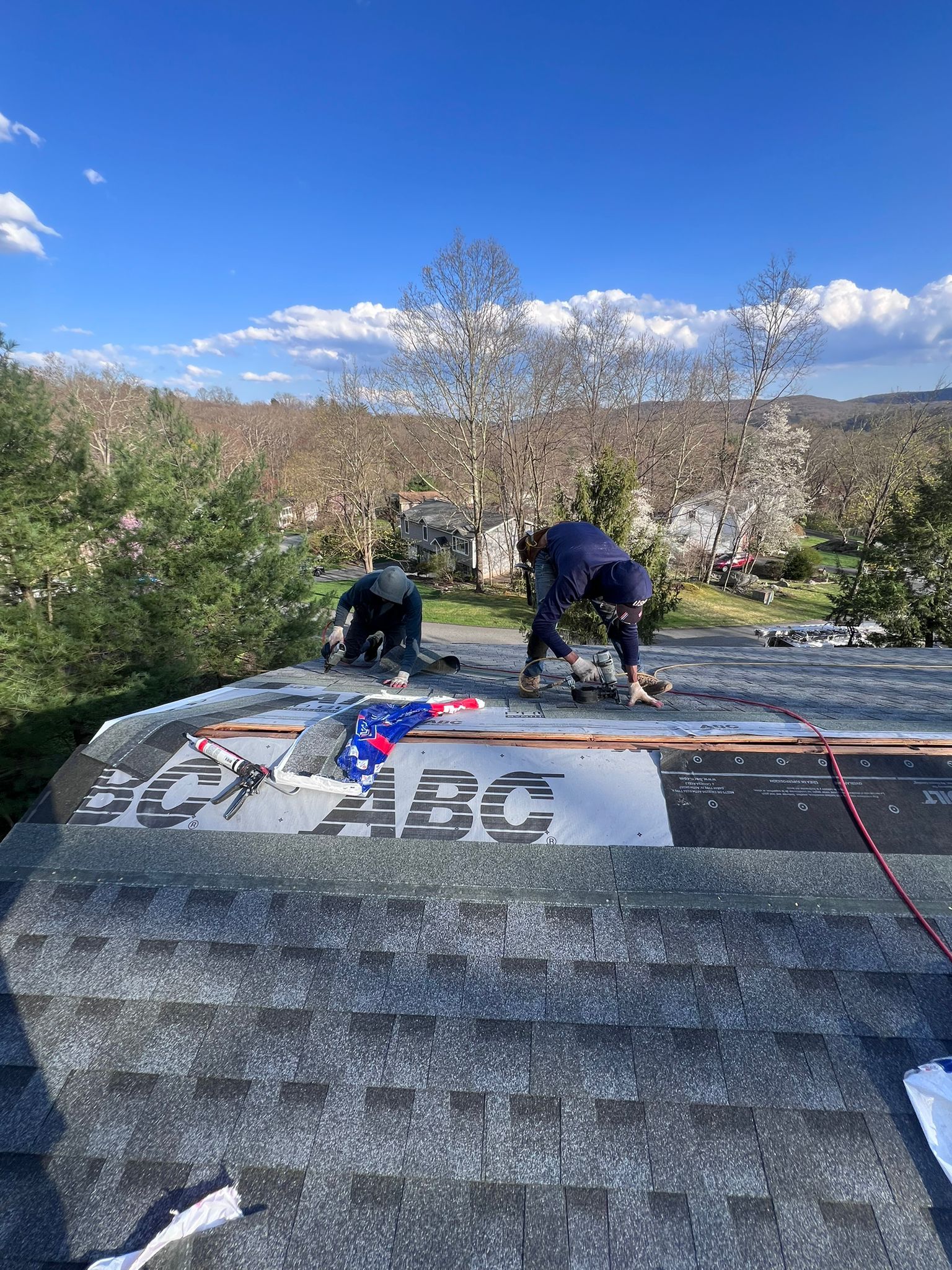 Three workers installing shingles on a rooftop on a sunny day.