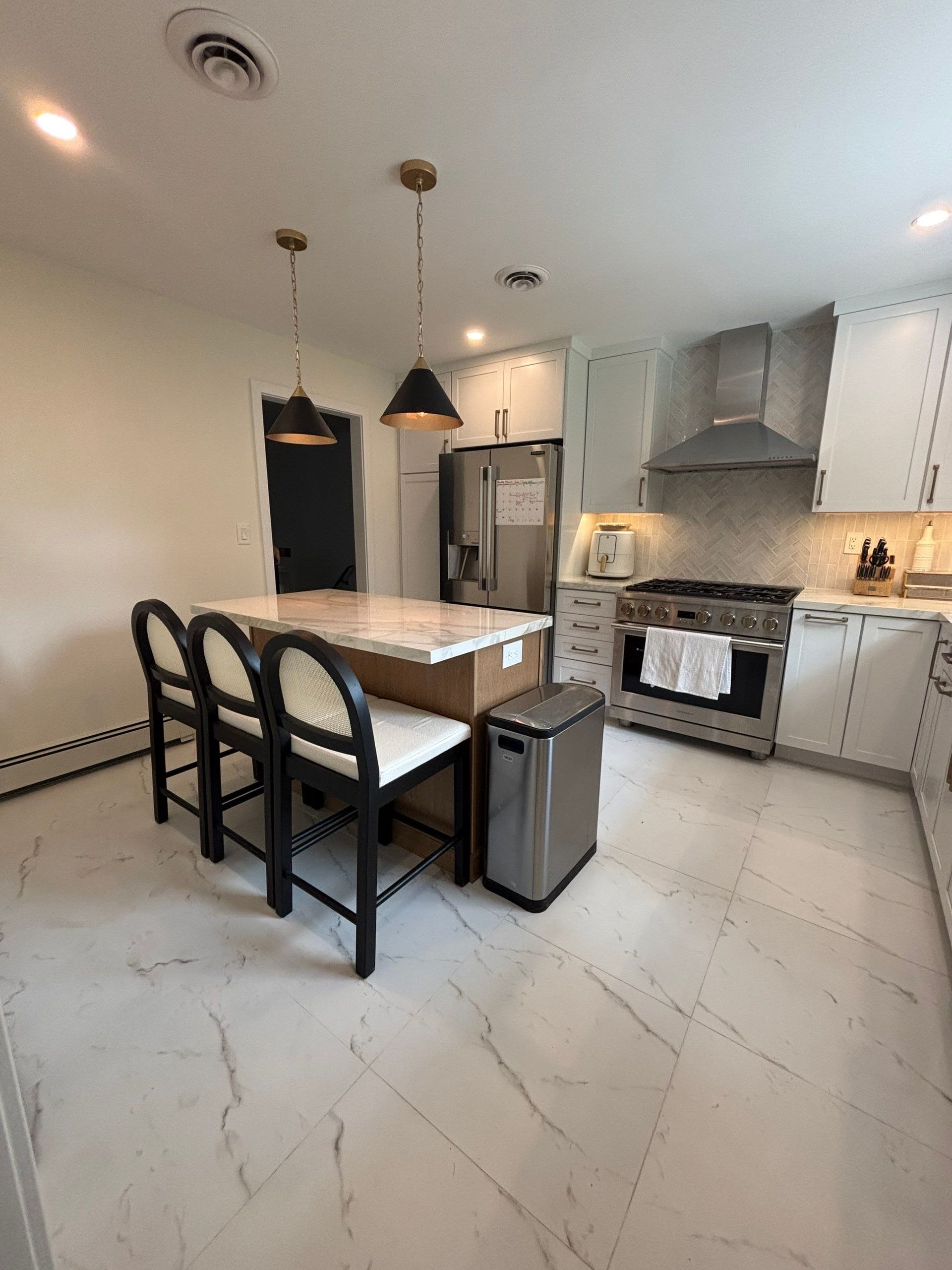Modern kitchen with white cabinets, marble floors, island with seating, and stainless steel appliances.