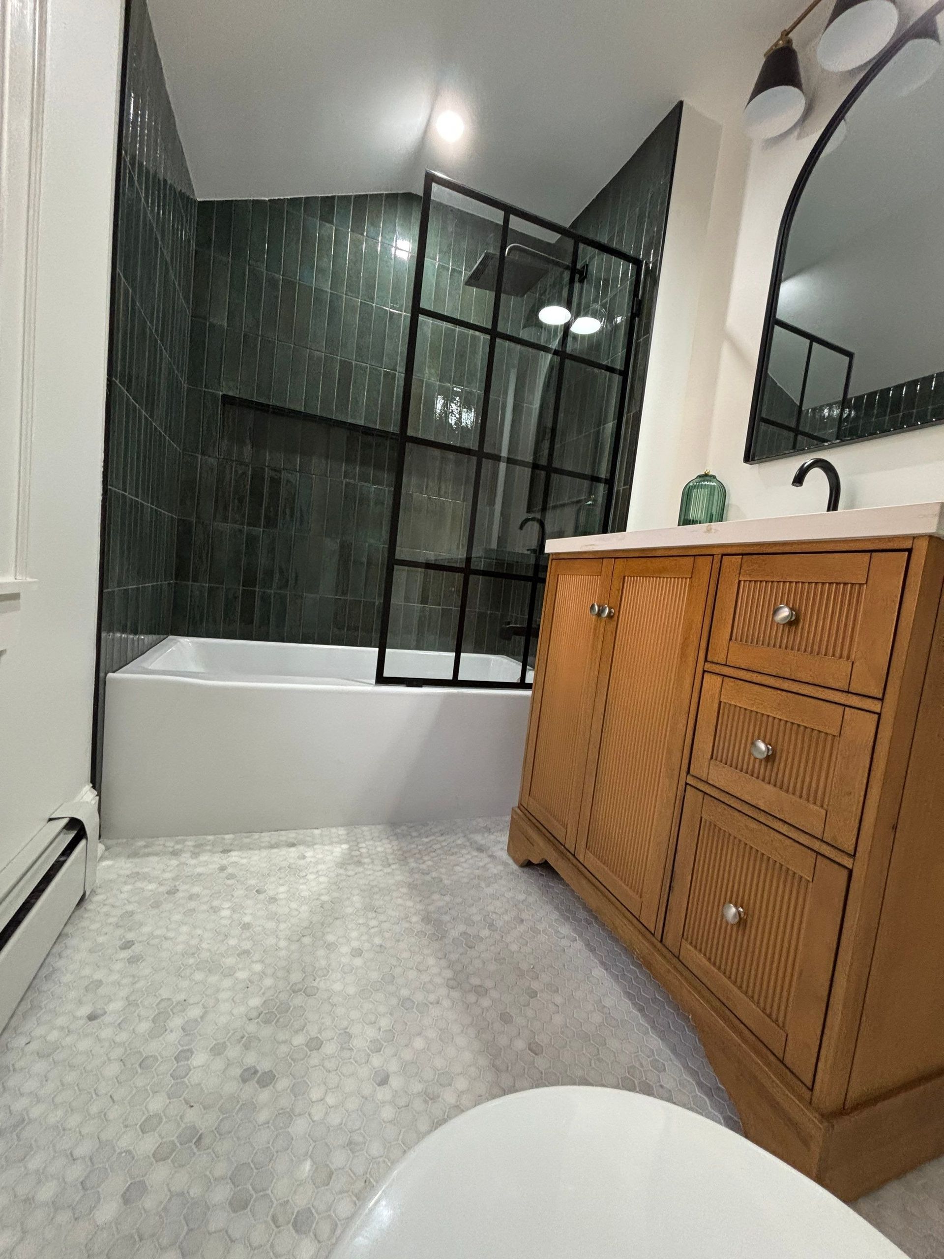Bathroom with green tiled shower, white tub, wooden vanity, and marble floor.