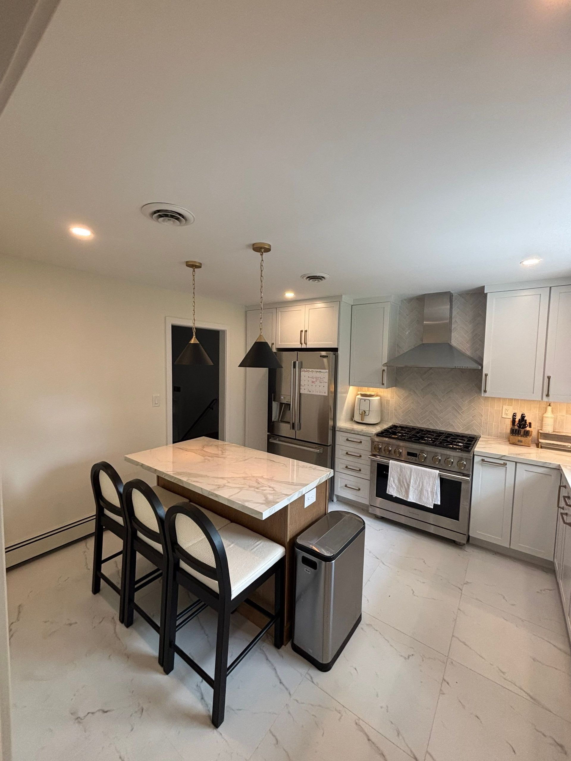 Modern kitchen with white cabinets, marble counters, island with seating, and stainless steel appliances.