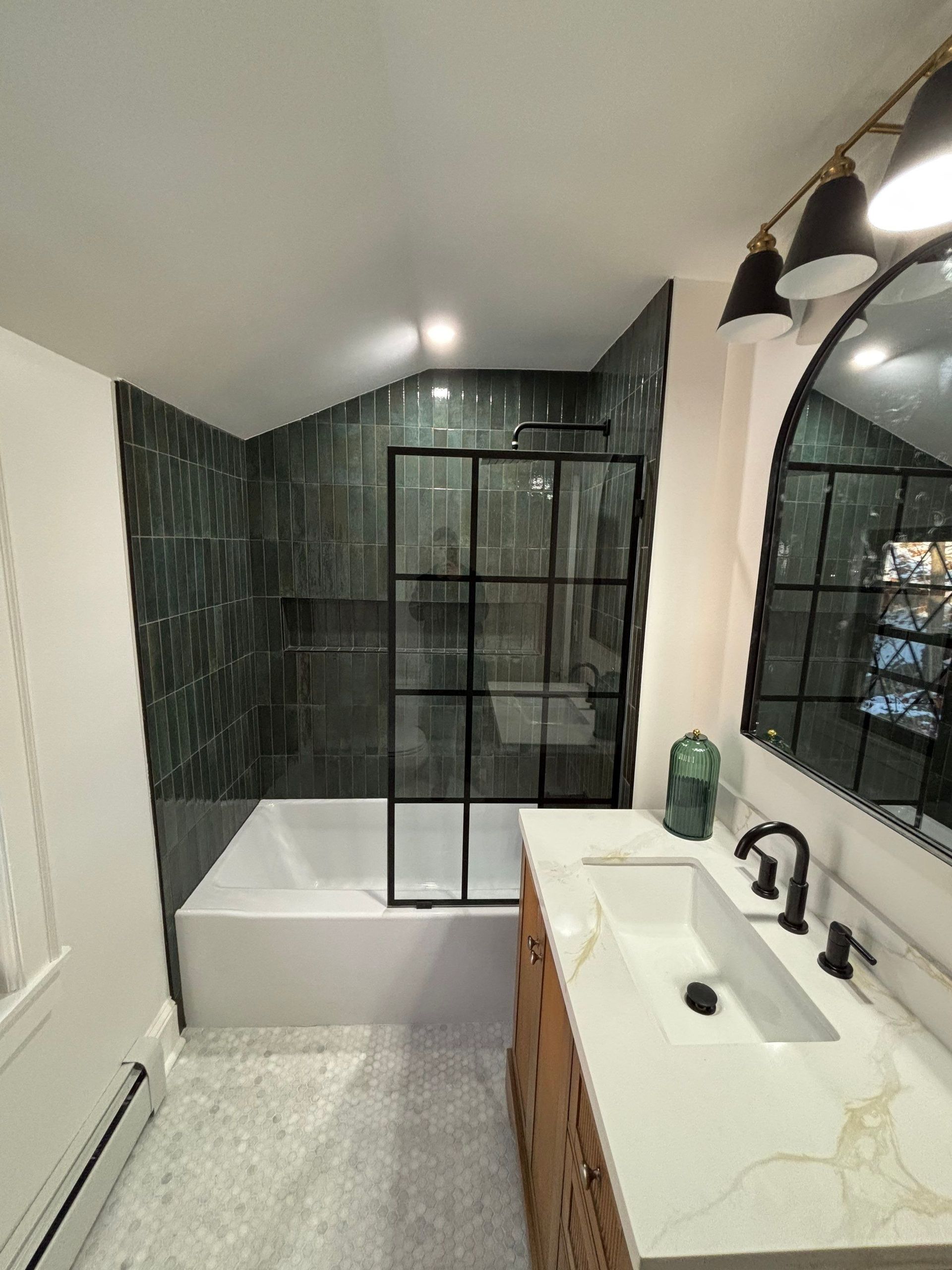 Modern bathroom with black-framed shower, green tile, white tub, vanity with black faucet and a large mirror.
