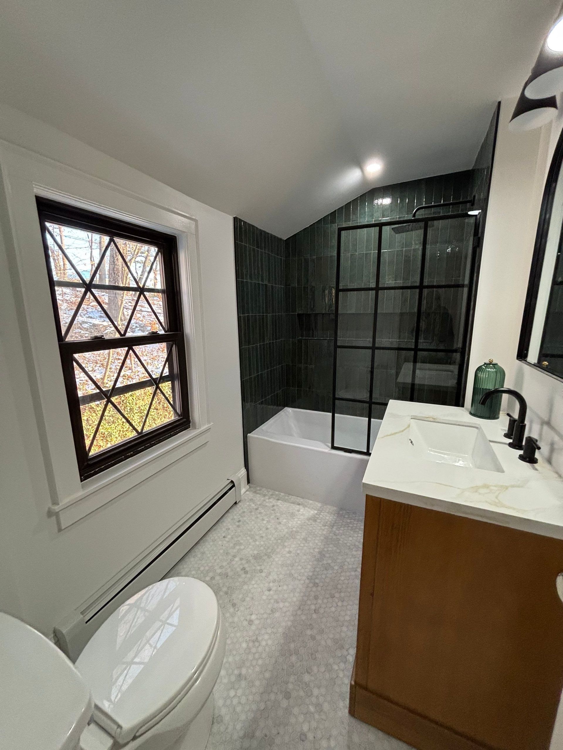 Newly renovated bathroom with dark green tiled shower, black-framed shower door, and white fixtures.