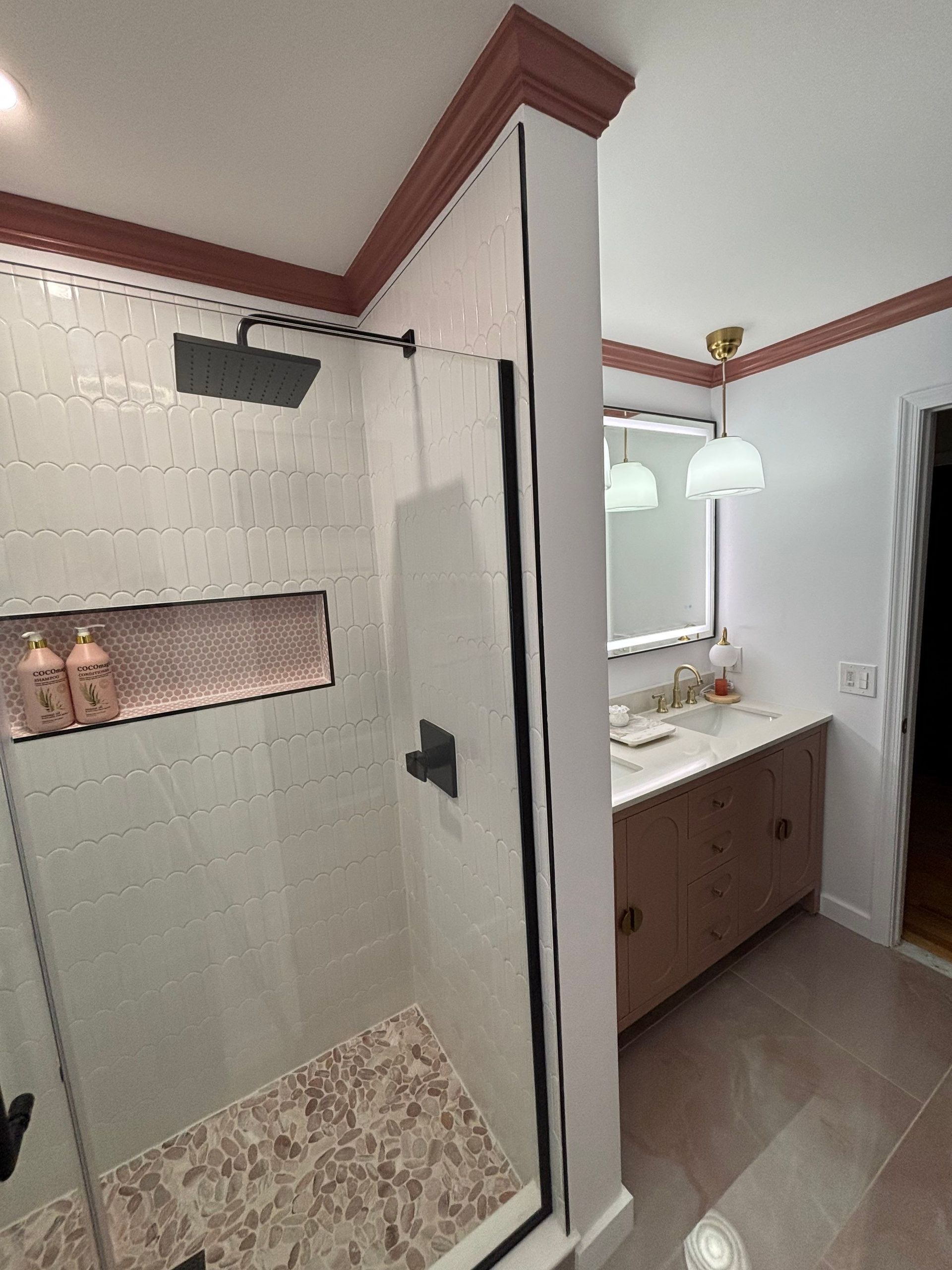 Bathroom with tiled shower, vanity, and overhead lighting. Rose-colored trim.