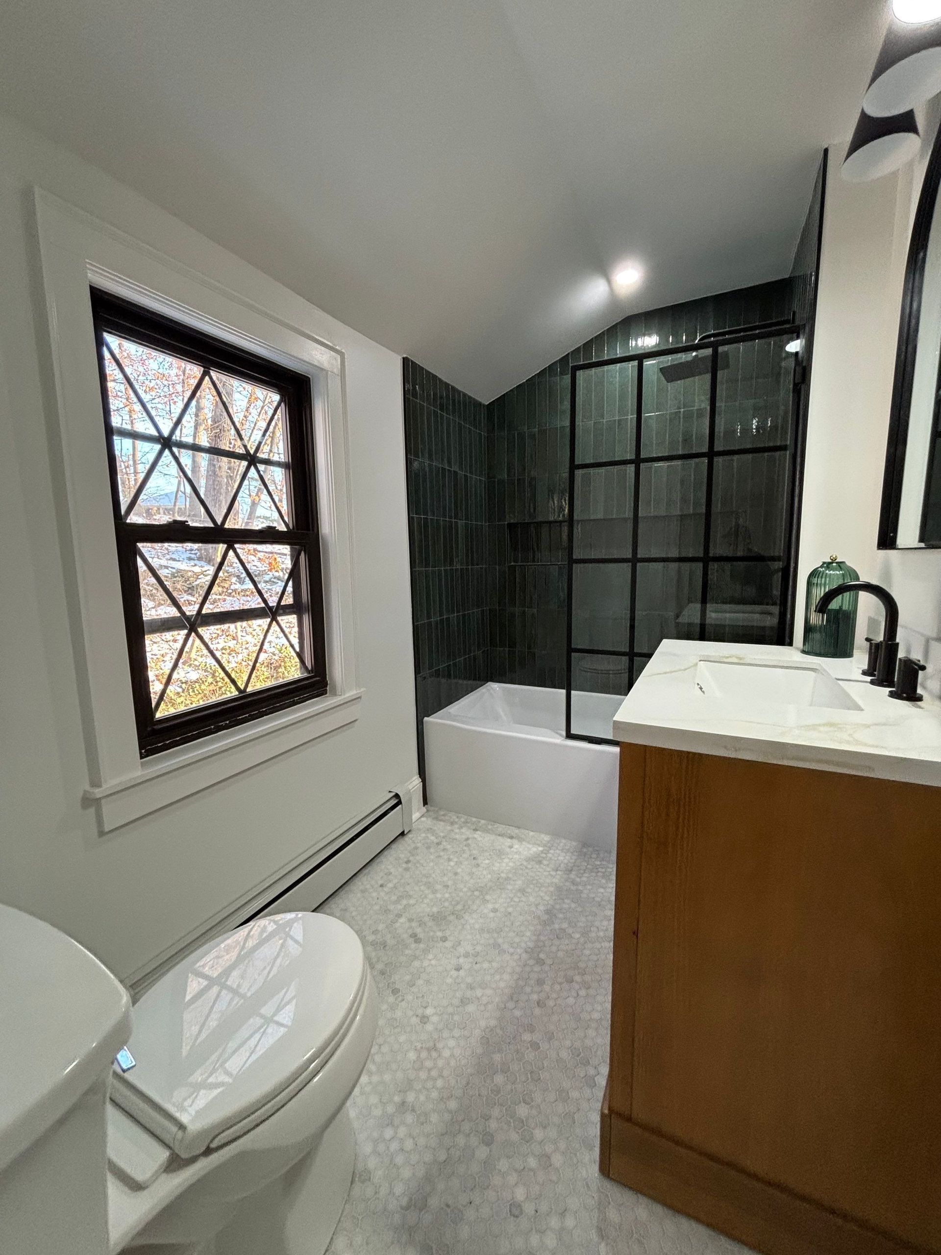 Bathroom with a toilet, vanity, and shower. The walls are white and the shower tiles are dark.