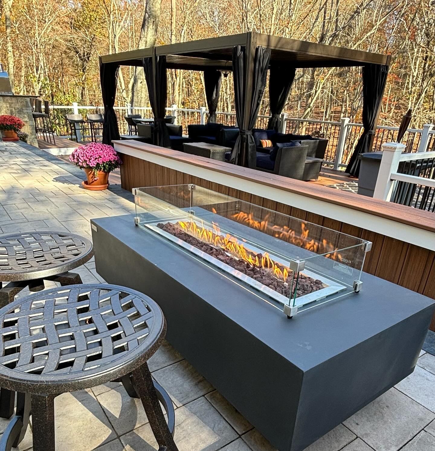 Outdoor patio with a modern fire pit, seating area with canopy, and two stools.