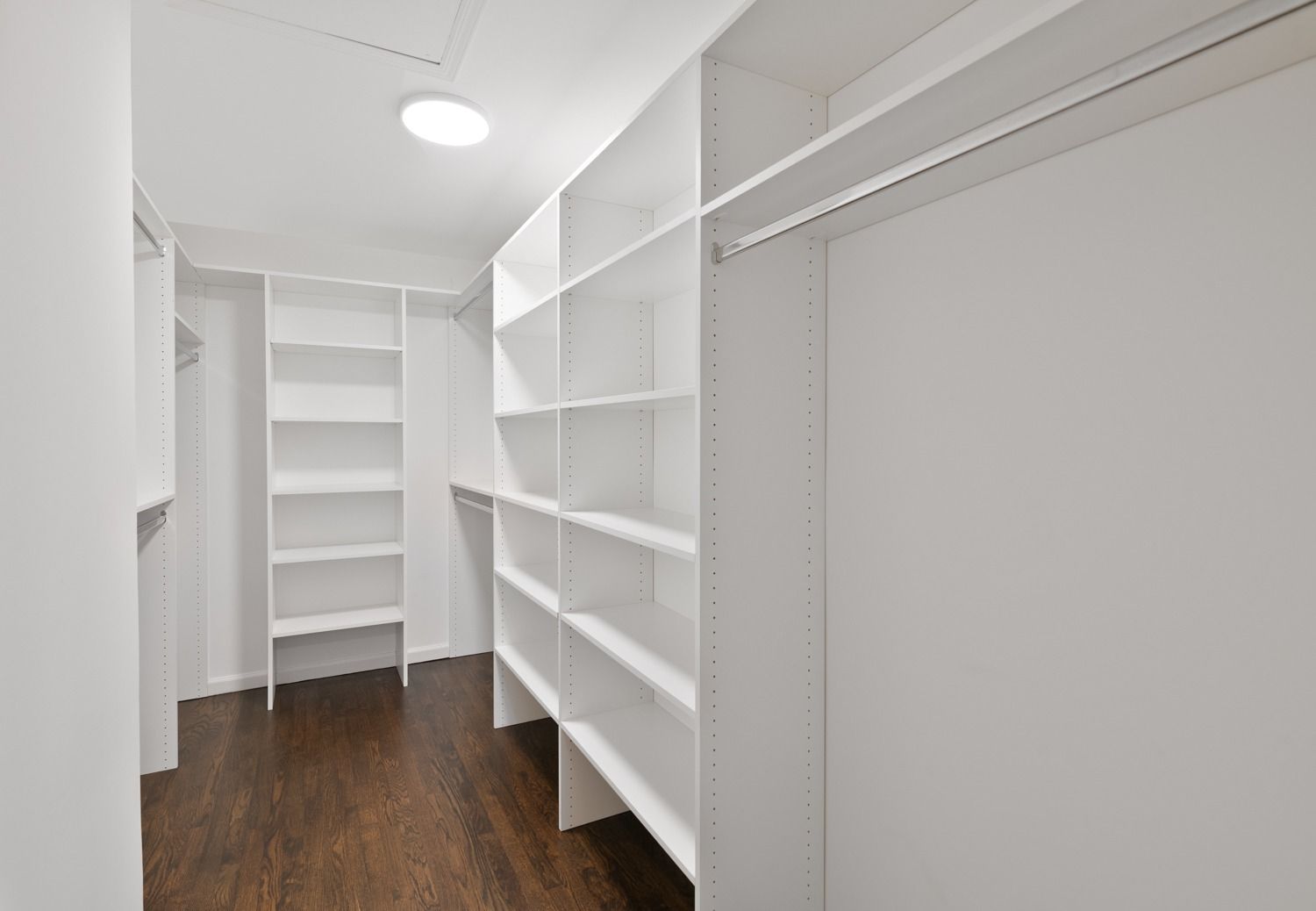 Empty walk-in closet with white shelves and dark wood floor.