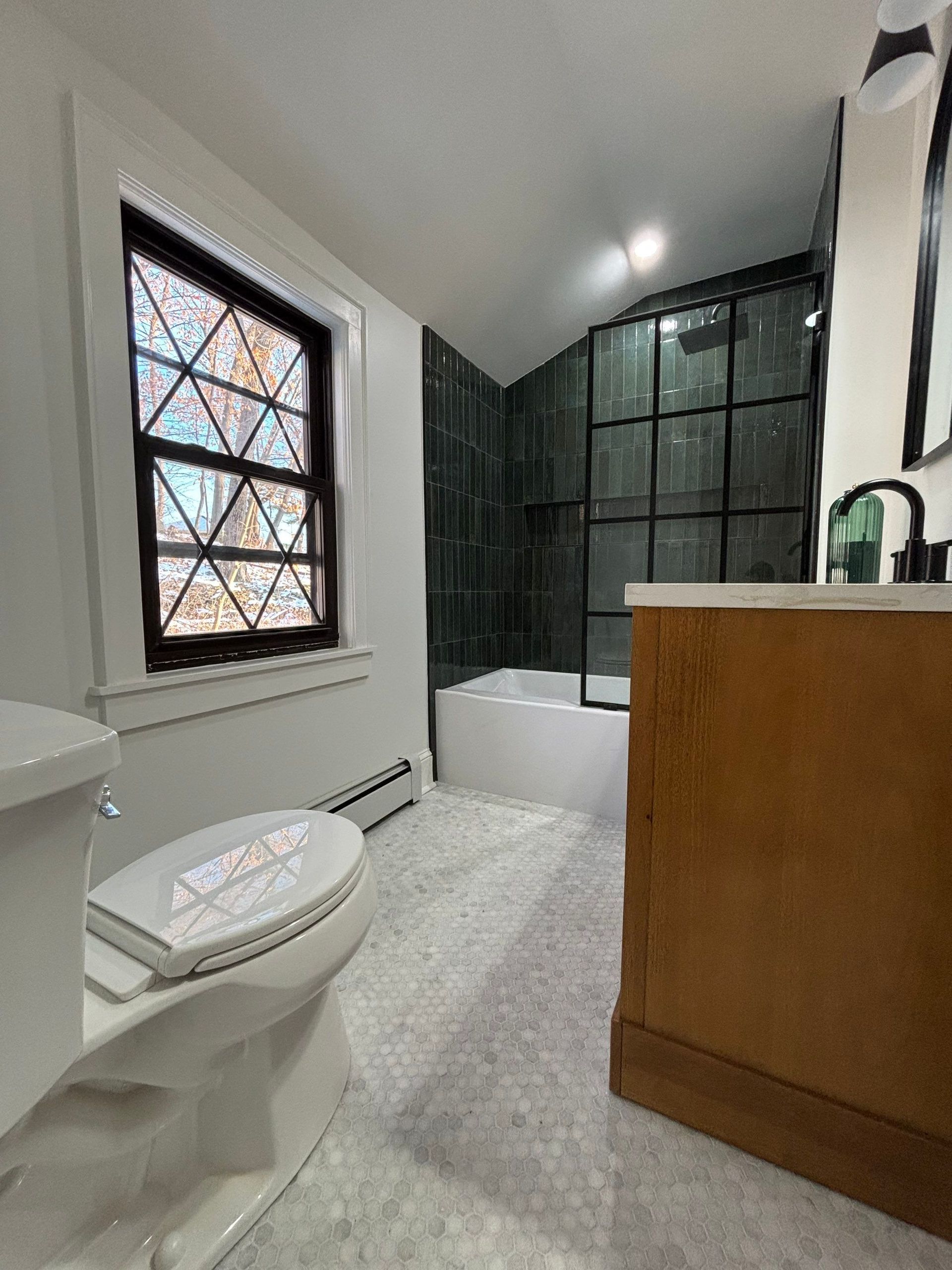 Bathroom with toilet, vanity, tub, black-framed shower, and stained-glass window.