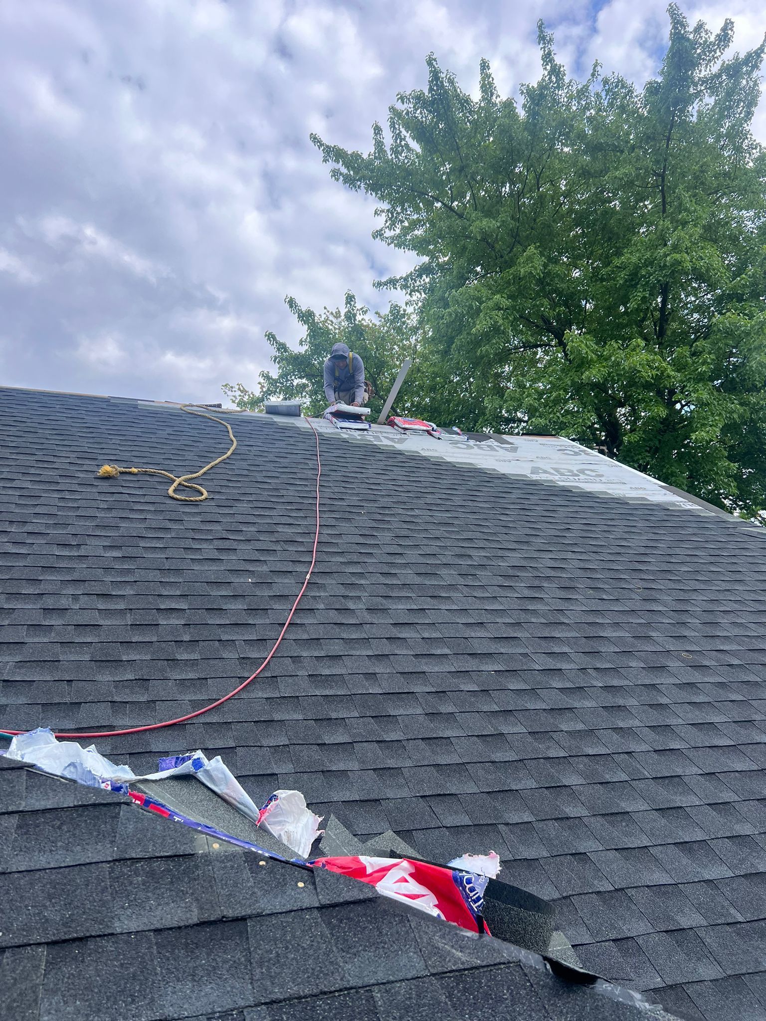 Rooftop with shingles being replaced. Partial blue sky, green tree. American flag debris visible.