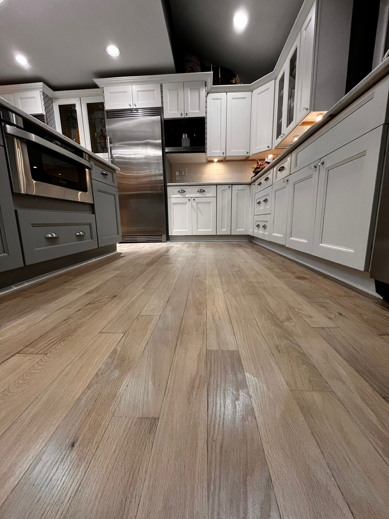 Kitchen with light wood floor, white cabinets, stainless steel appliances, and overhead lighting.