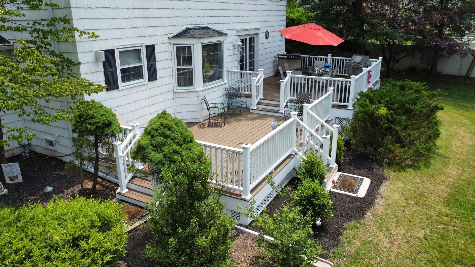 White house with a multi-level deck, red umbrella, and green yard.