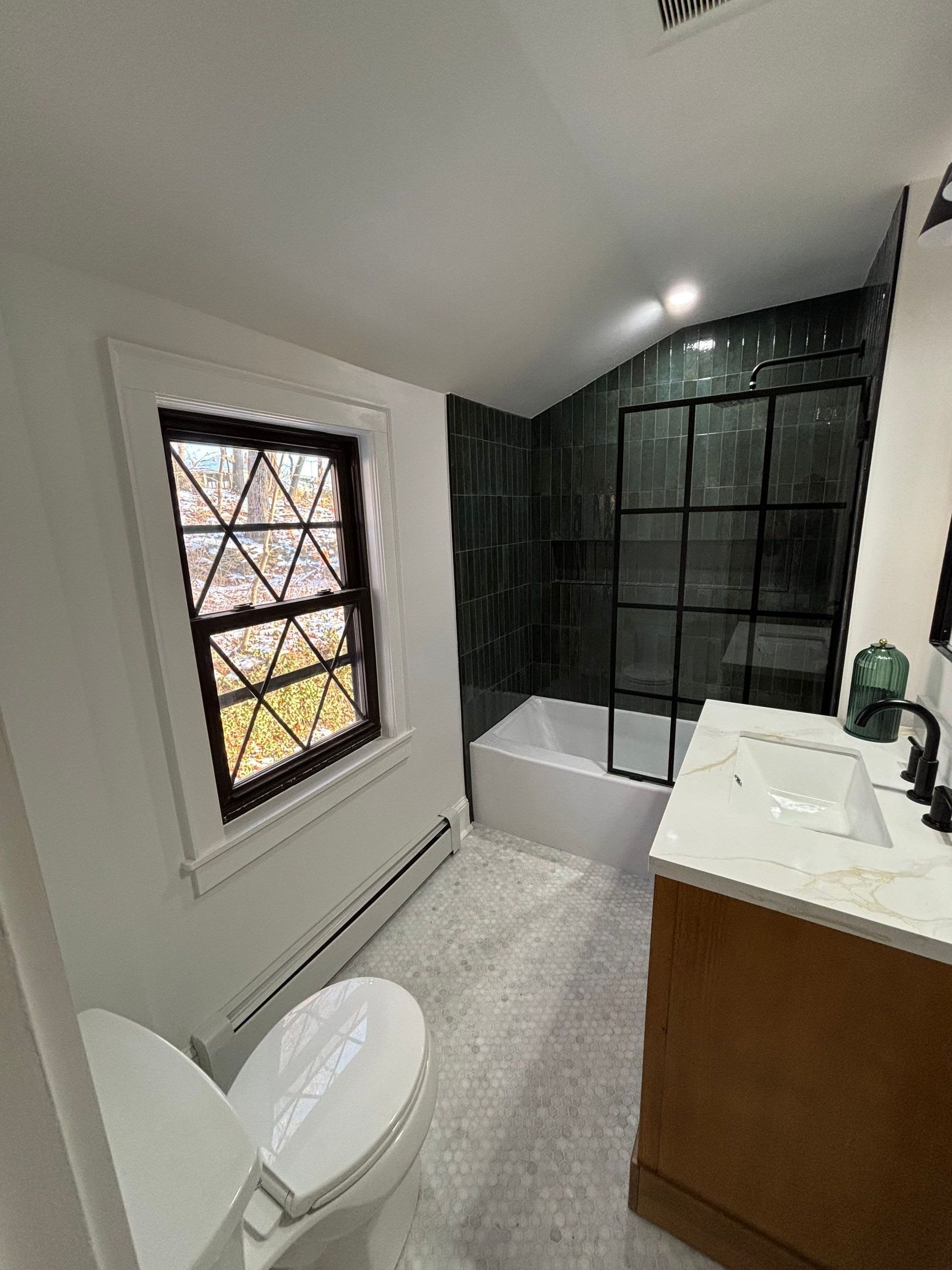 Bathroom with white walls, window, tub with black shower screen, vanity, and toilet.