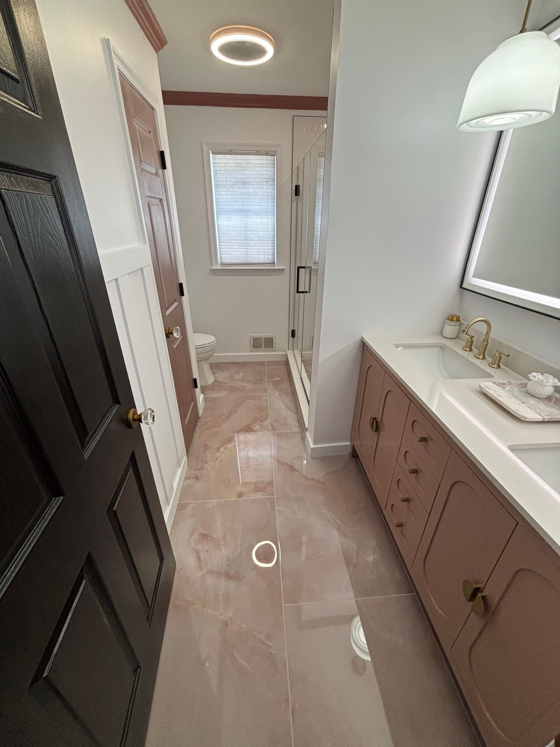 Bathroom interior with pink tiled floor, vanity, shower, toilet, and black door.