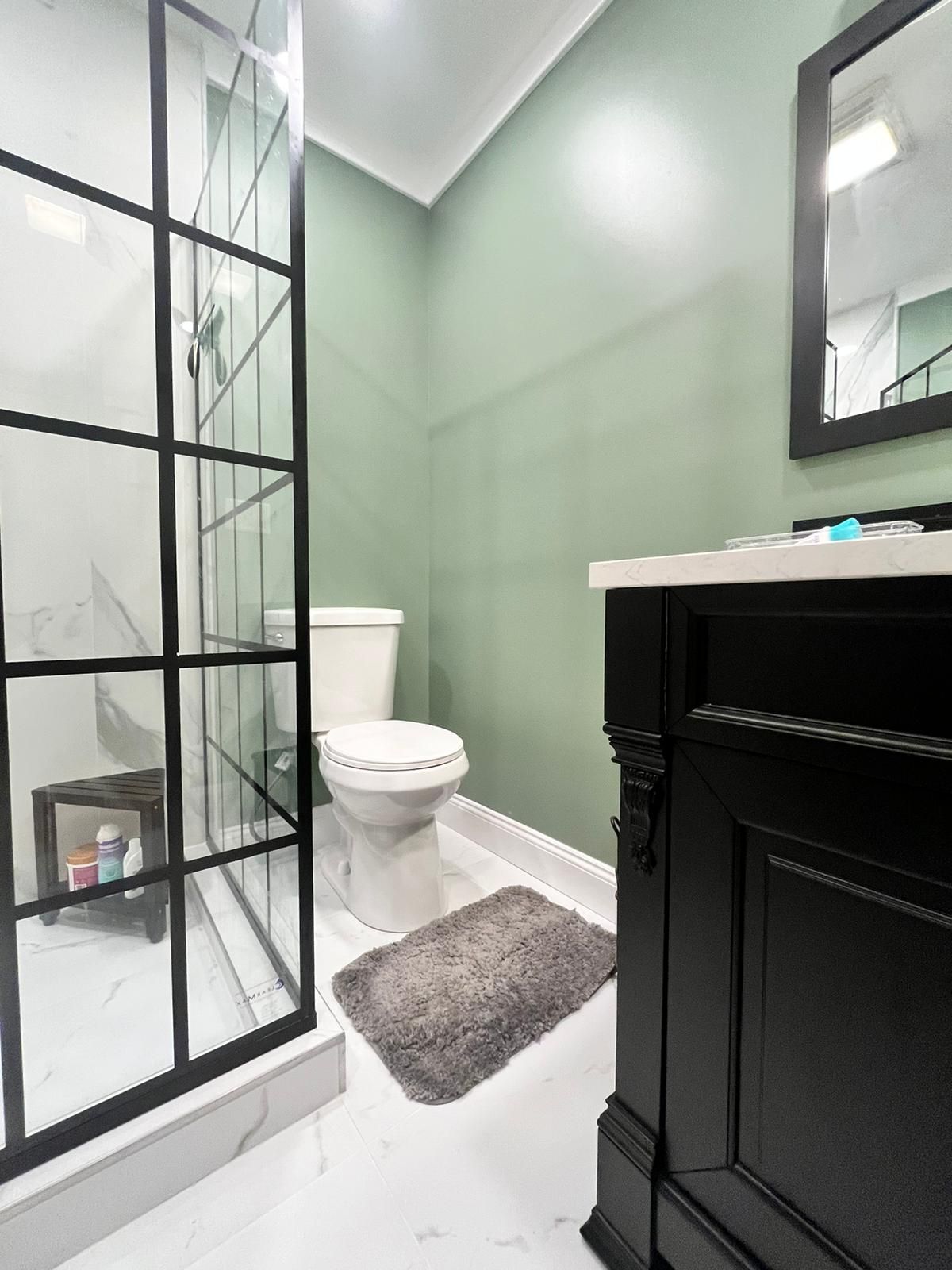 Bathroom with green walls, a black vanity, a glass shower, and white tile flooring.