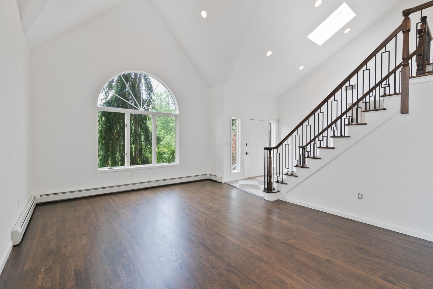 Empty, bright entryway with wood floor, large arched window, and staircase.
