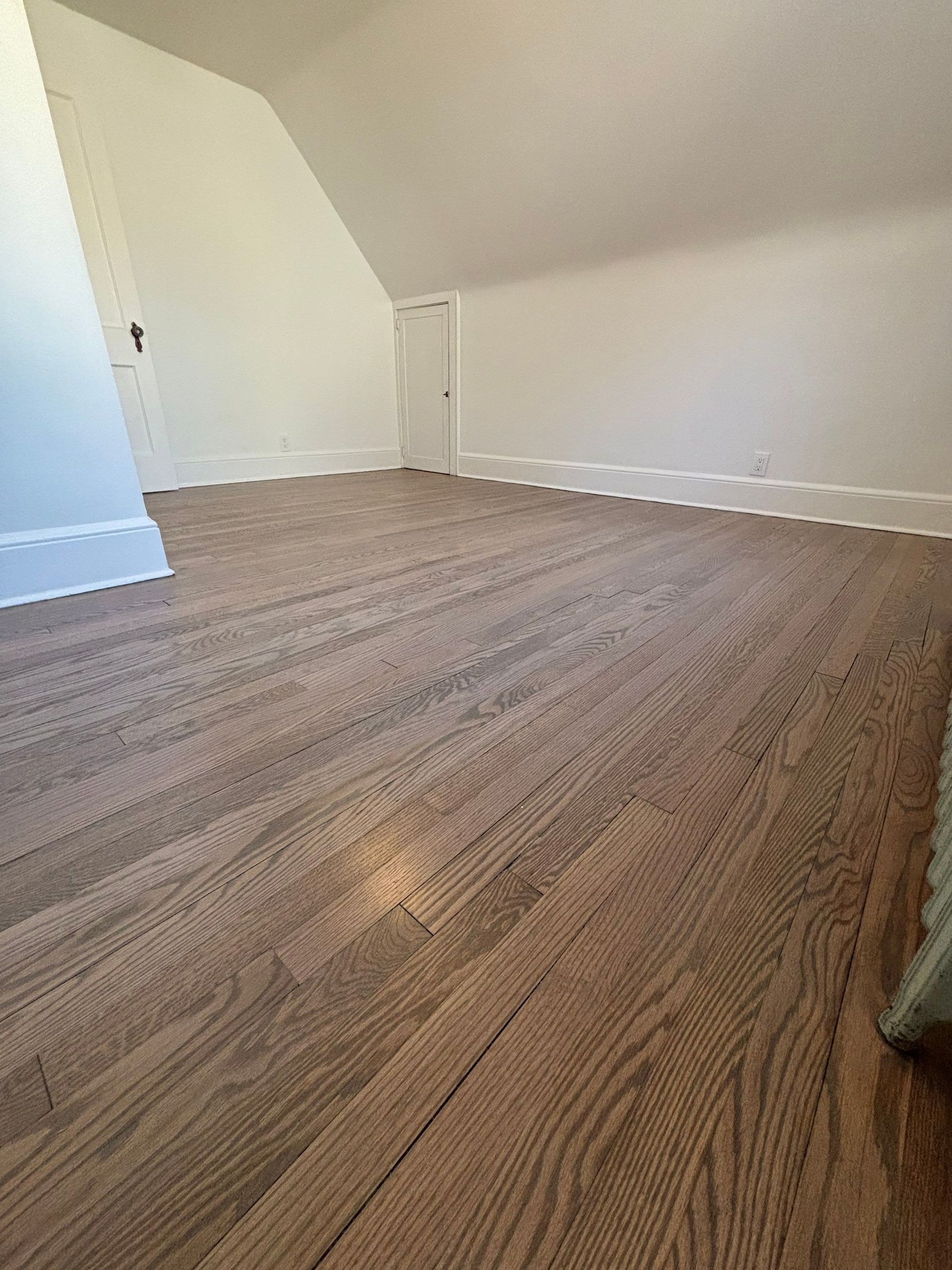 Wooden floor in a room with white walls and slanted ceiling.