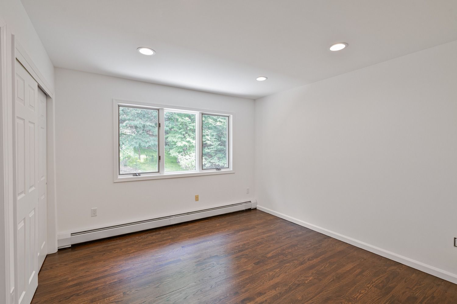 Empty room with three windows, hardwood floor, white walls, and closet door.