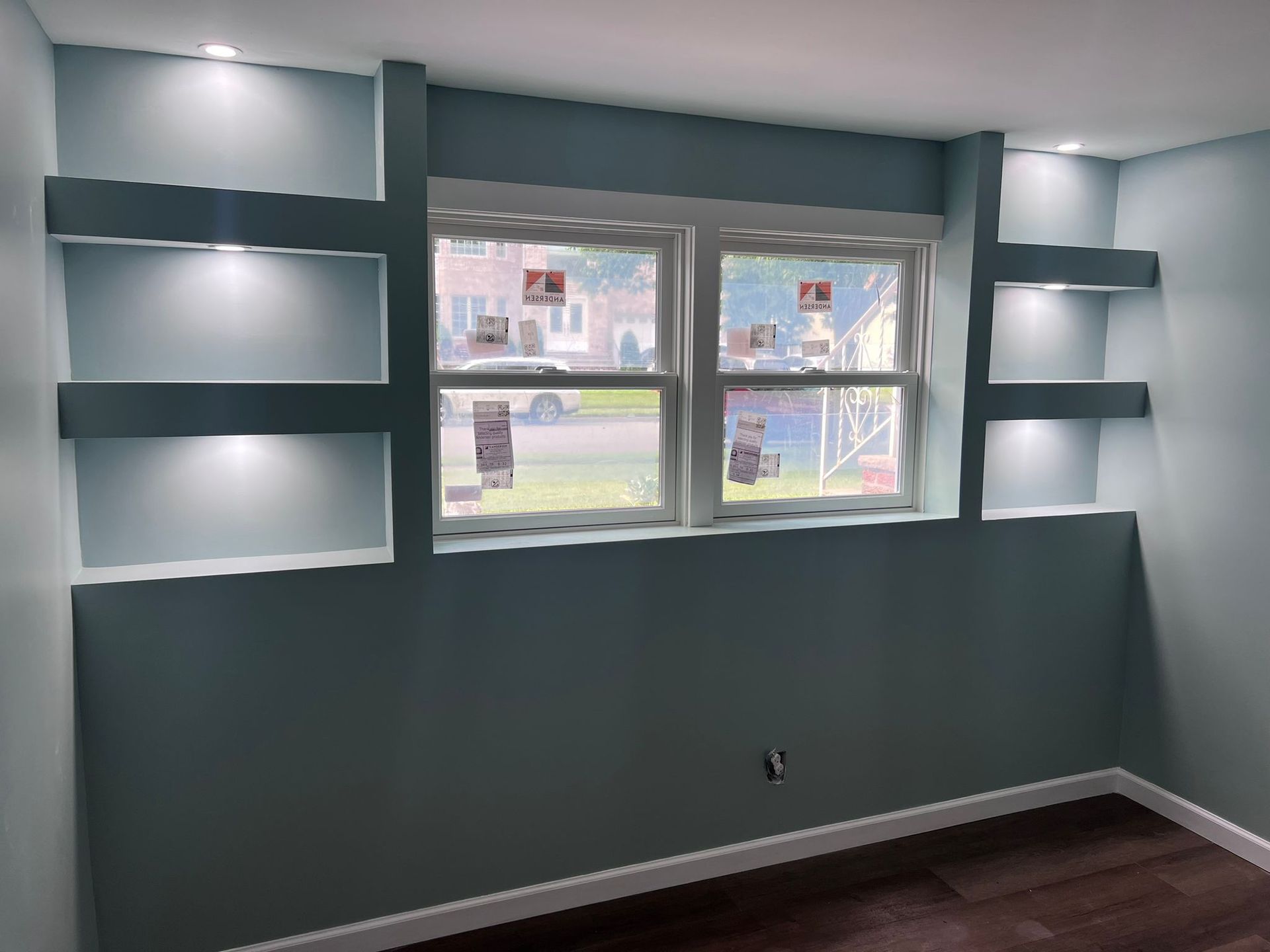Blue wall with window, built-in lit shelves. Brown flooring.
