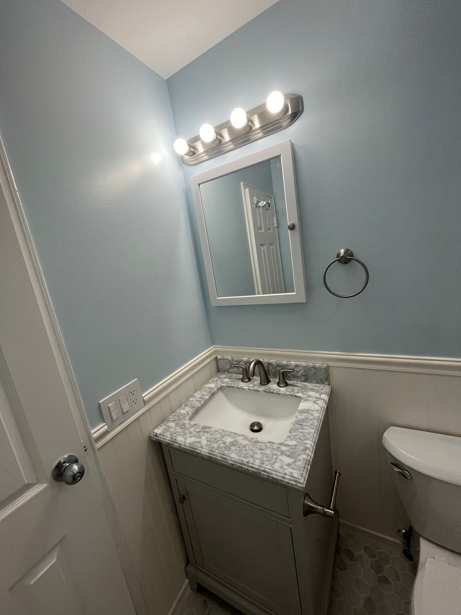 Bathroom with blue walls, white trim, vanity with marble top, mirror, and toilet.