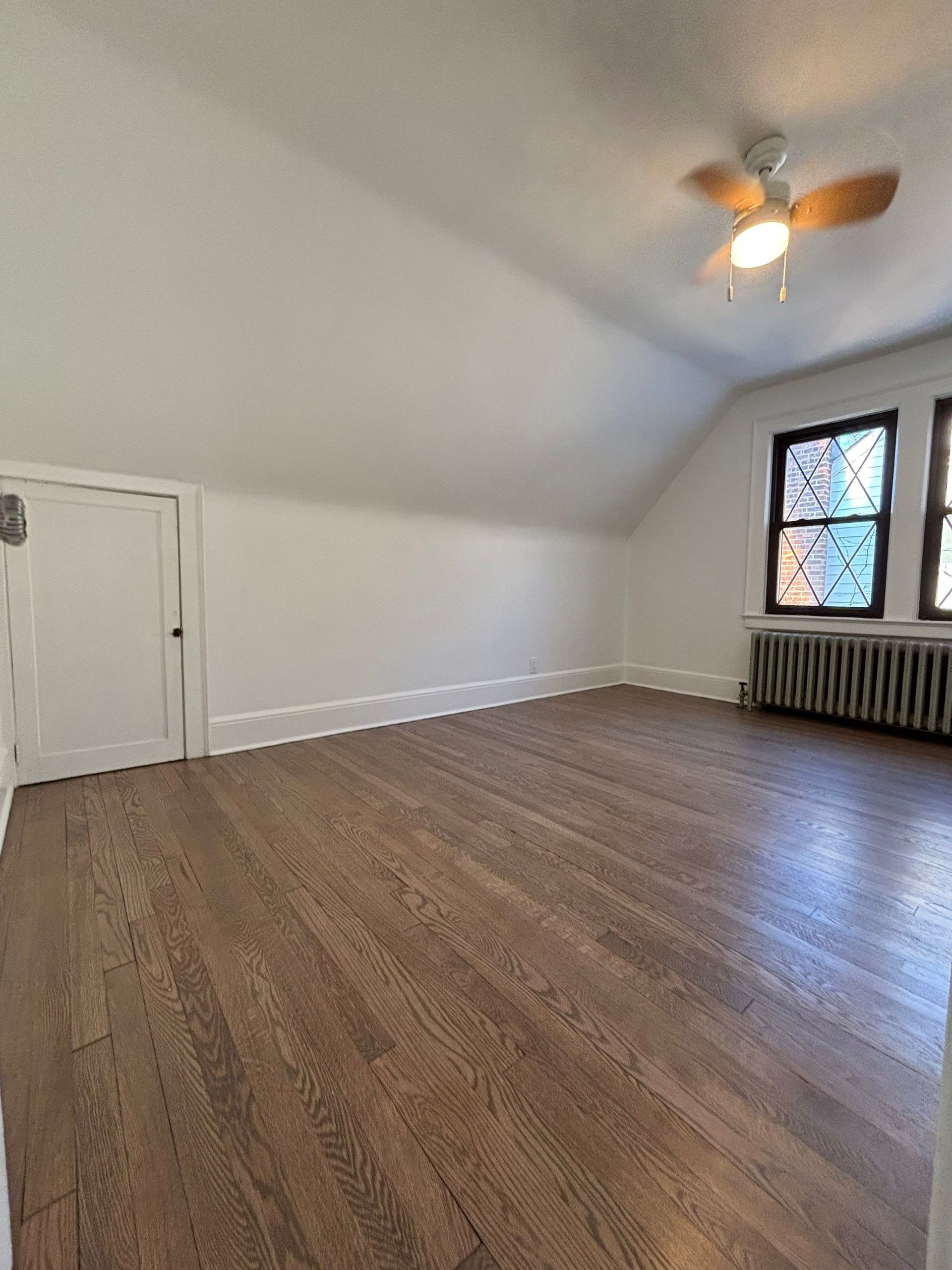 Empty room with sloped ceiling, hardwood floor, white walls, and two stained glass windows.